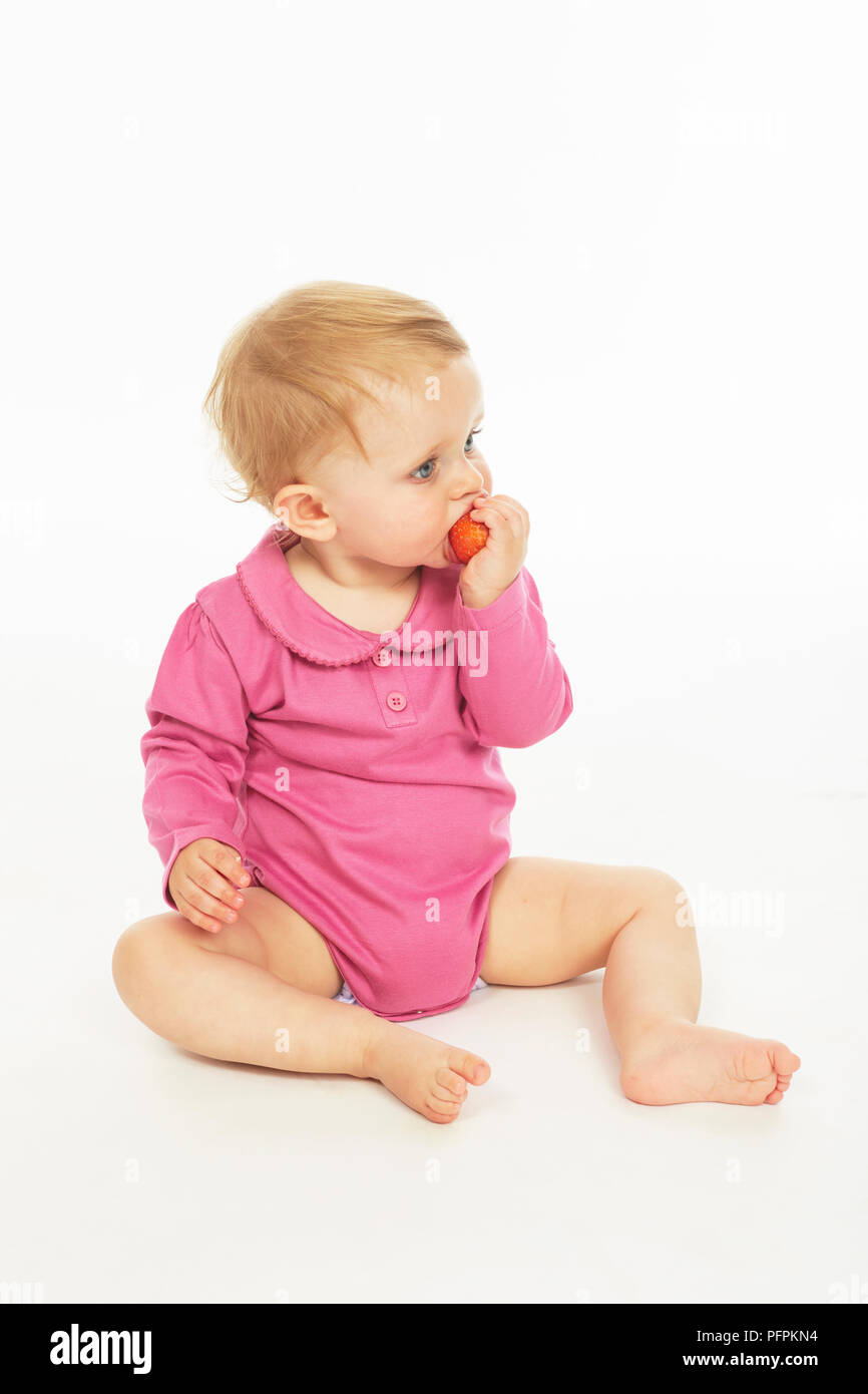 Bébé en monokini rose eating strawberry (modèle age - 9 mois) Banque D'Images