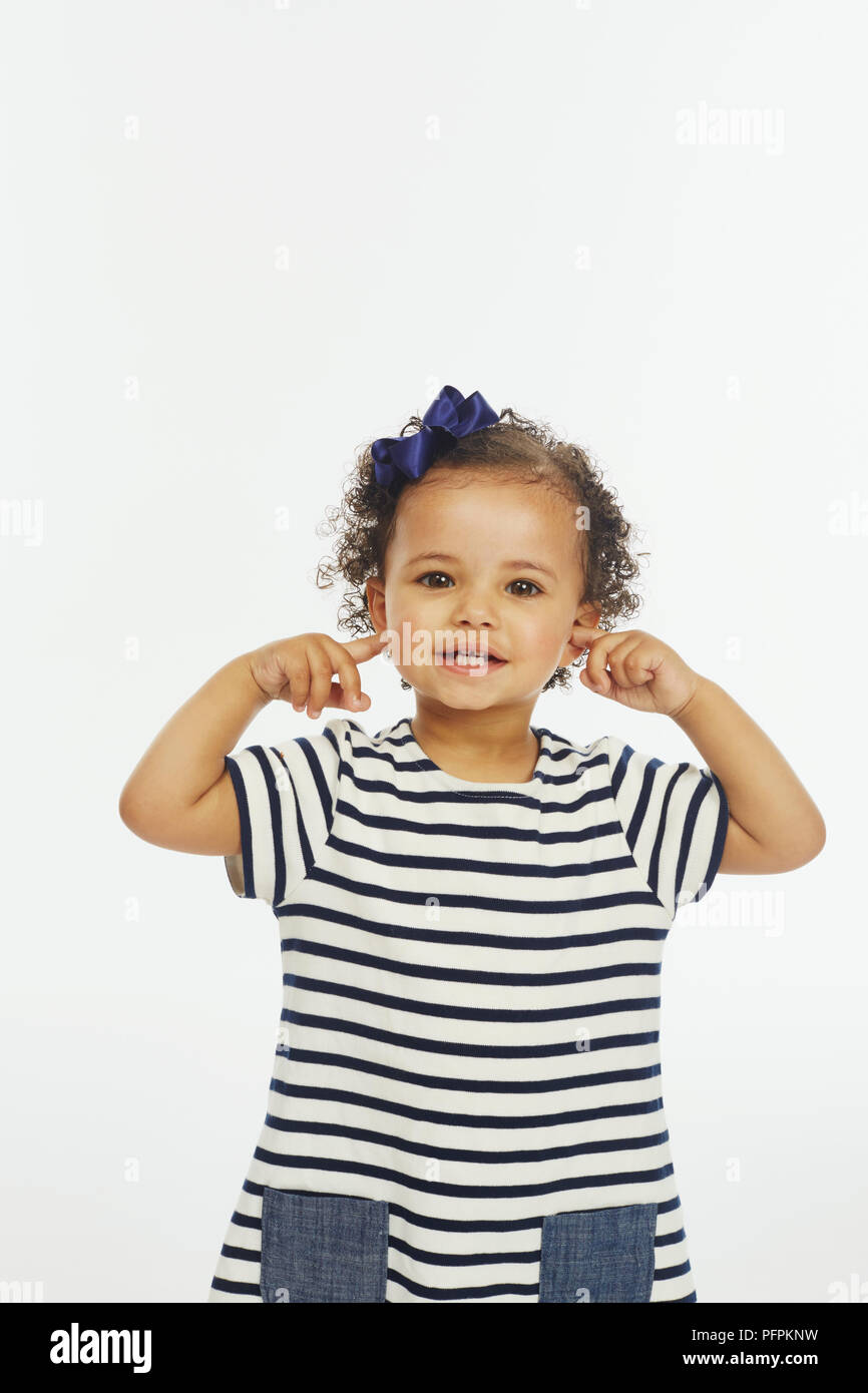 Petite fille en robe stripey en pointant sur les oreilles (Modèle âge - 19 mois) Banque D'Images