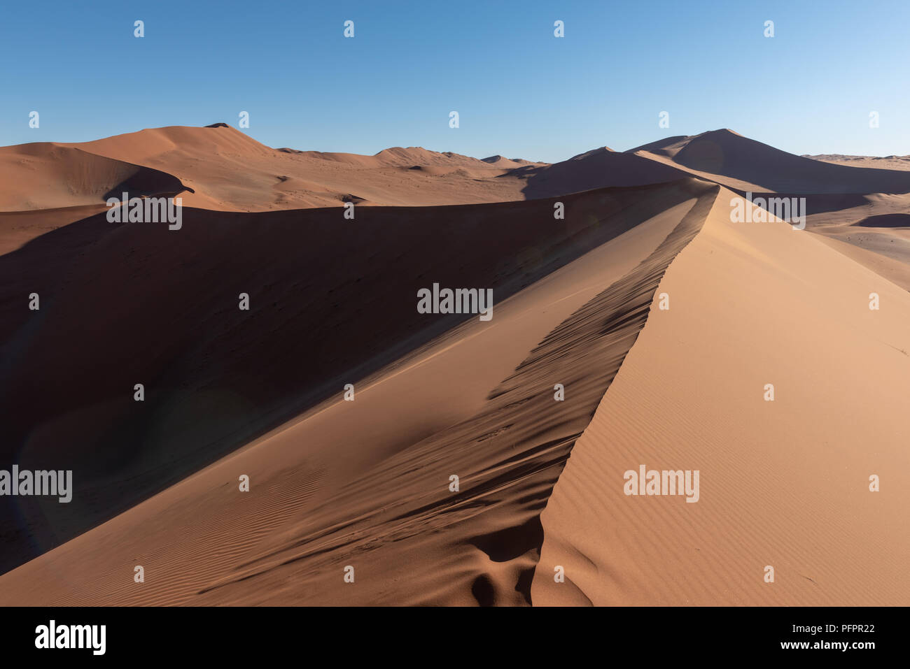 Belle vue sur la dune du haut d'une dune de sable rouge dans le désert de Namib avec sun flare et de ciel bleu, l'aventure randonnées, Namibie Banque D'Images