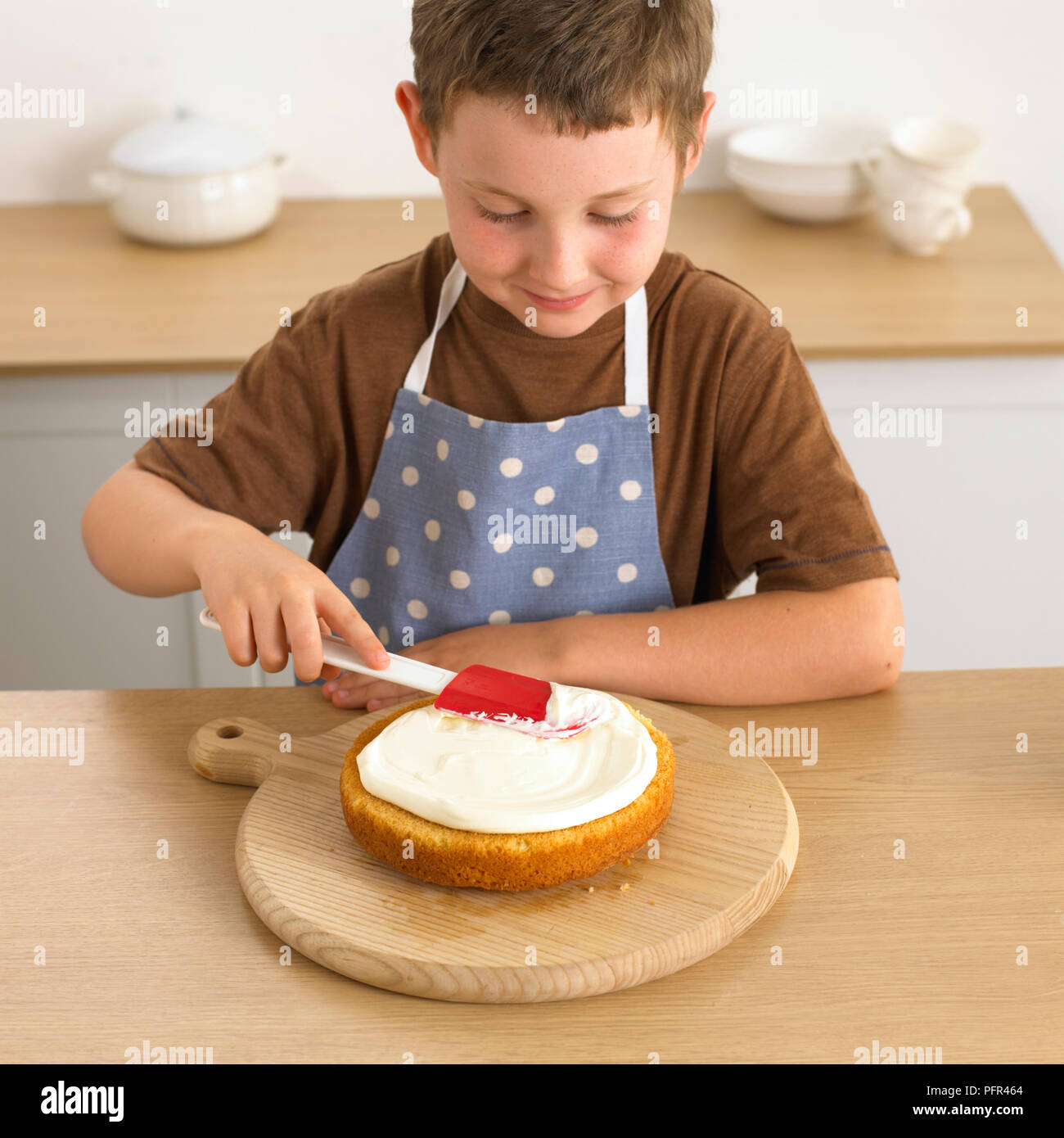 Boy diffusion de crème sur le gâteau éponge avec une spatule, 8 ans Banque D'Images
