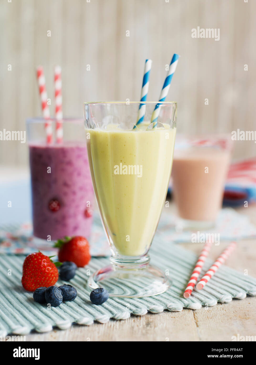 Lunettes avec pailles contenant divers smoothies aux fruits, banane et mangue en premier plan, et de fraises et de bleuets en arrière Banque D'Images