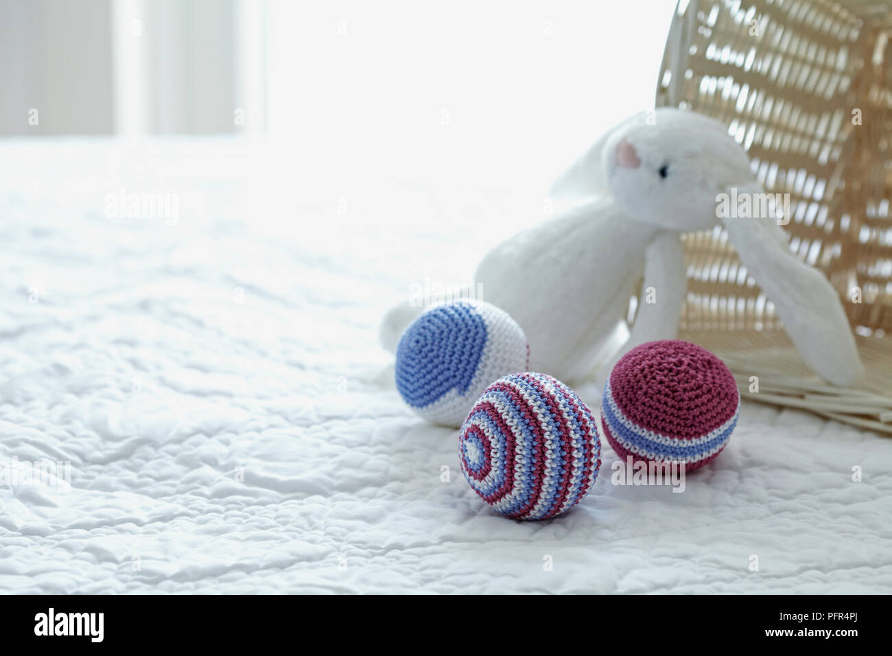 Boules de jouet en bonneterie et lapin en peluche sur un lit Banque D'Images