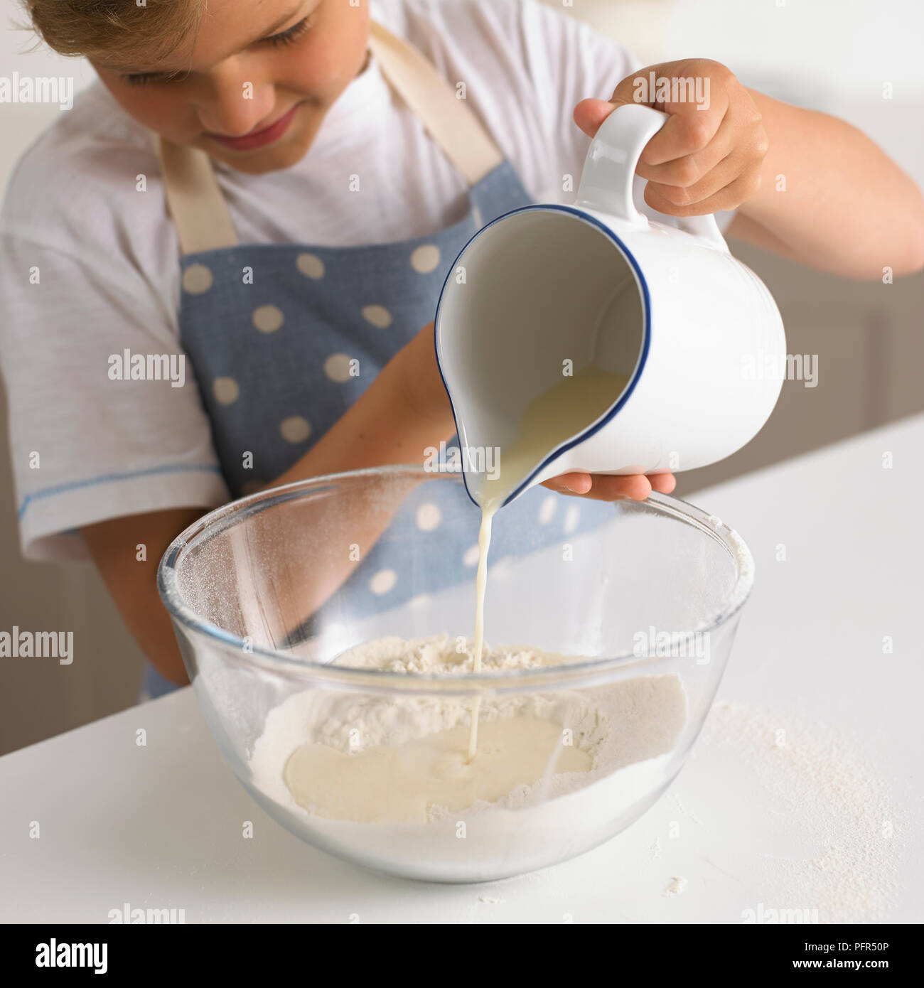 Faire de la pâte à crêpes, verser le lait dans le bol de farine, 6 ans Banque D'Images