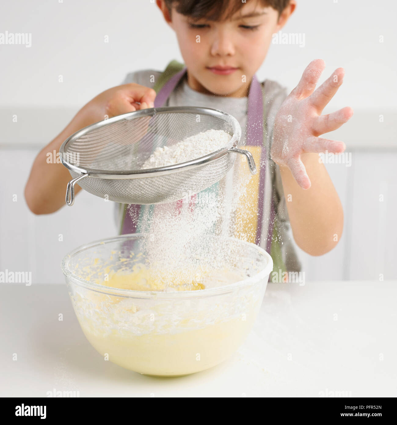 Garçon tamisant la farine sur un bol de mélange à gâteau, 7 ans Banque D'Images