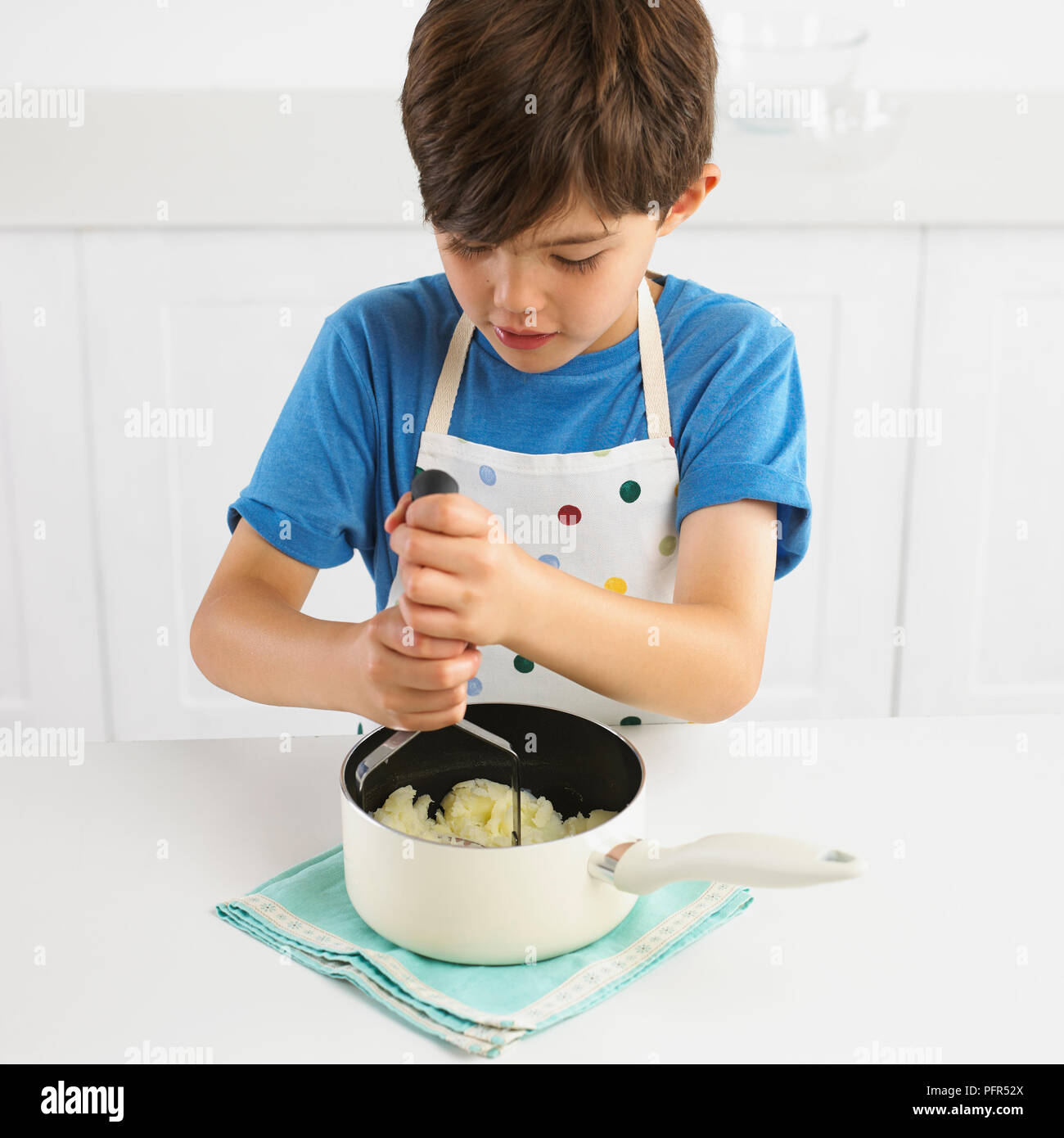 Garçon purée des pommes de terre dans une casserole, 7 ans Banque D'Images