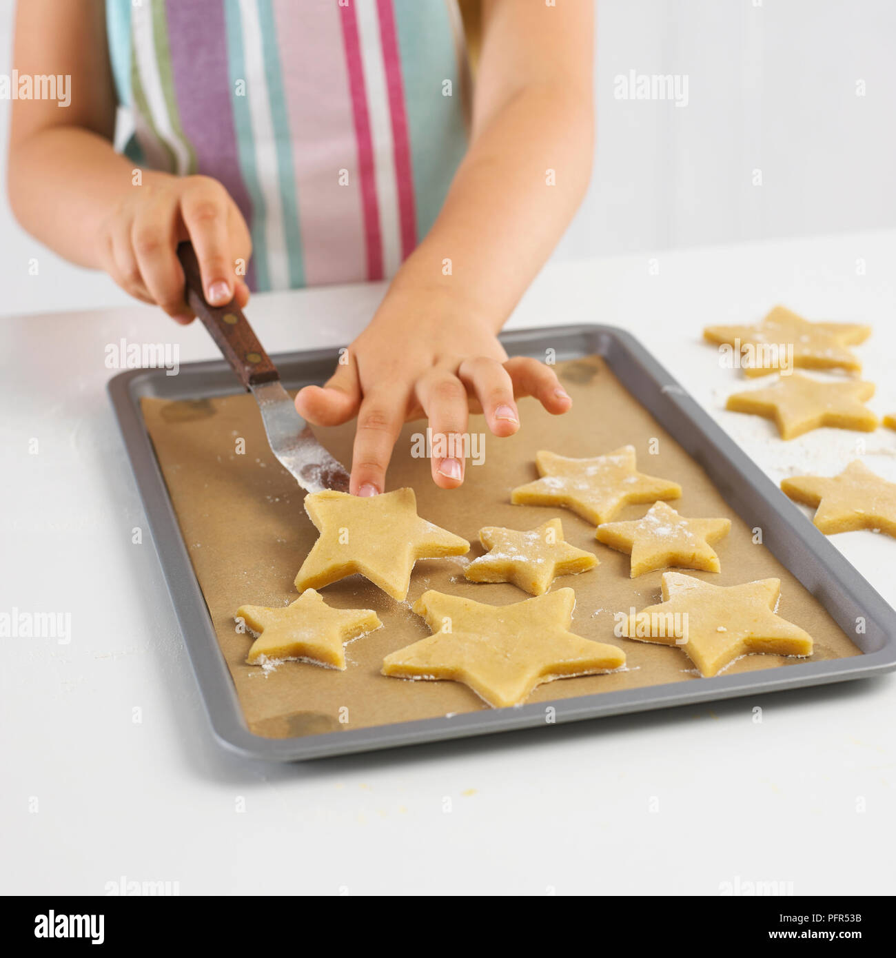 La mise en forme d'étoile de fille non cuit les cookies sur une plaque de cuisson, 5 ans Banque D'Images