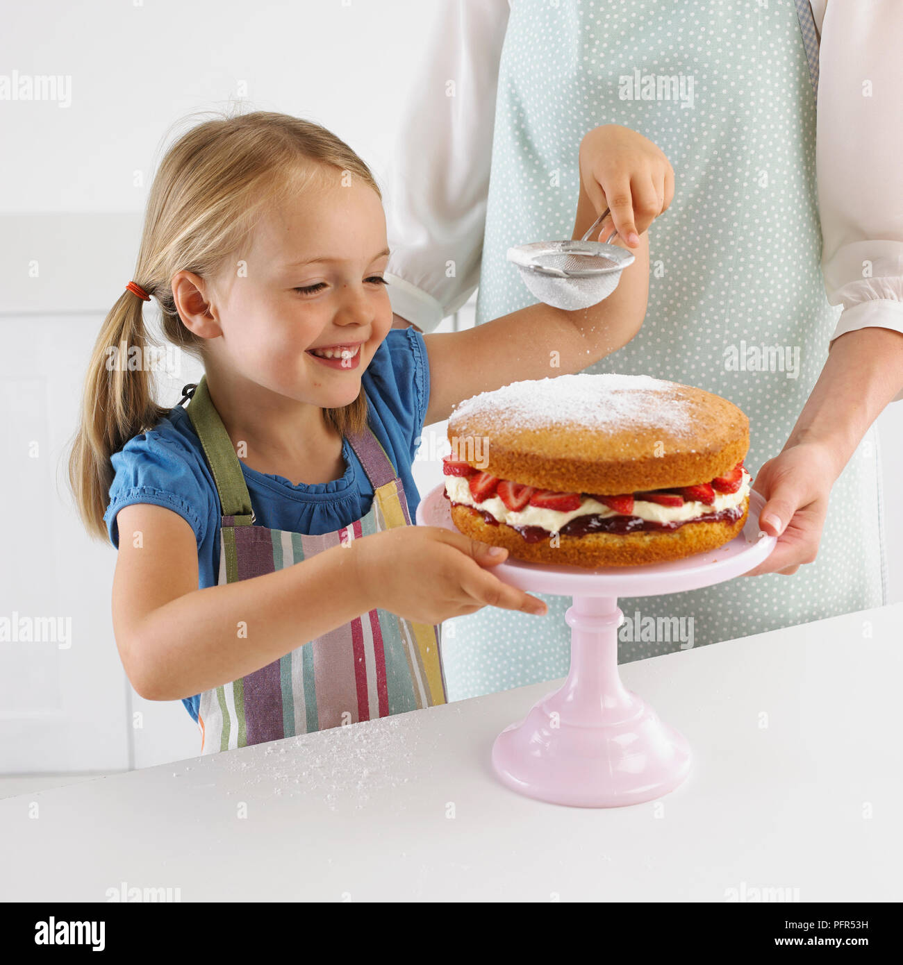 Smiling girl tamisant le sucre à glacer sur une fraise éponge, 5 ans Banque D'Images