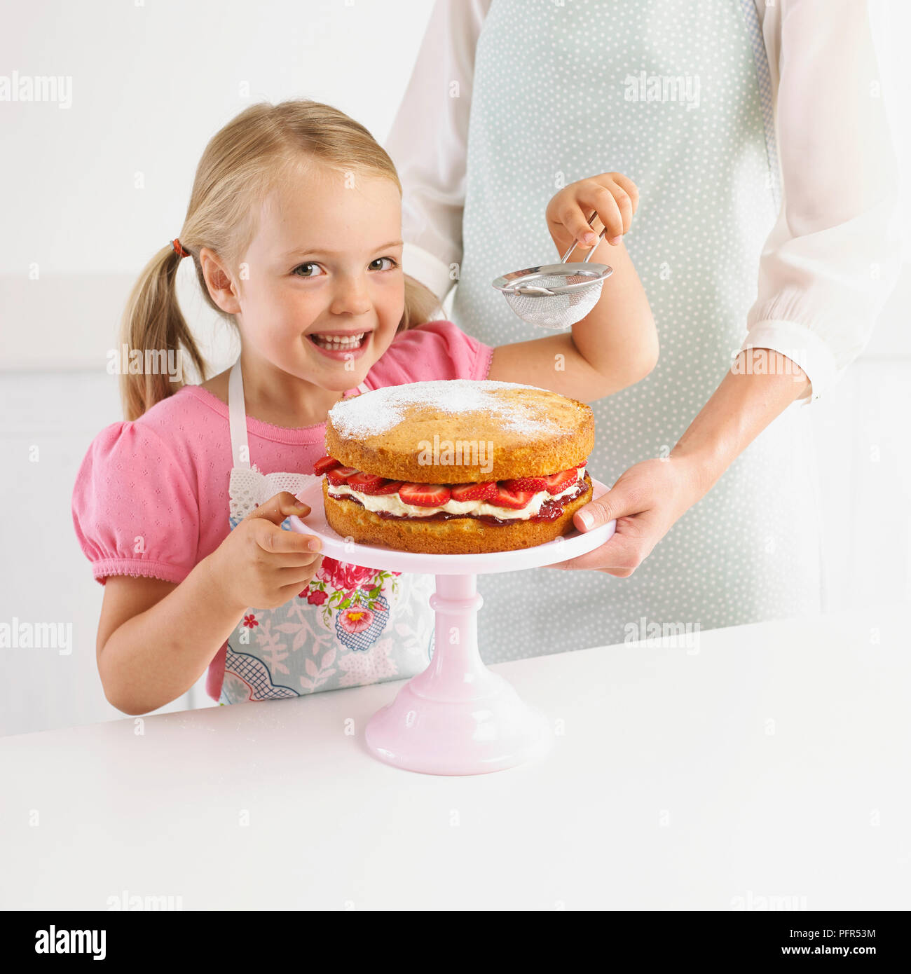 Smiling girl tamisant sucre à glacer gâteau aux fraises, 5 ans Banque D'Images