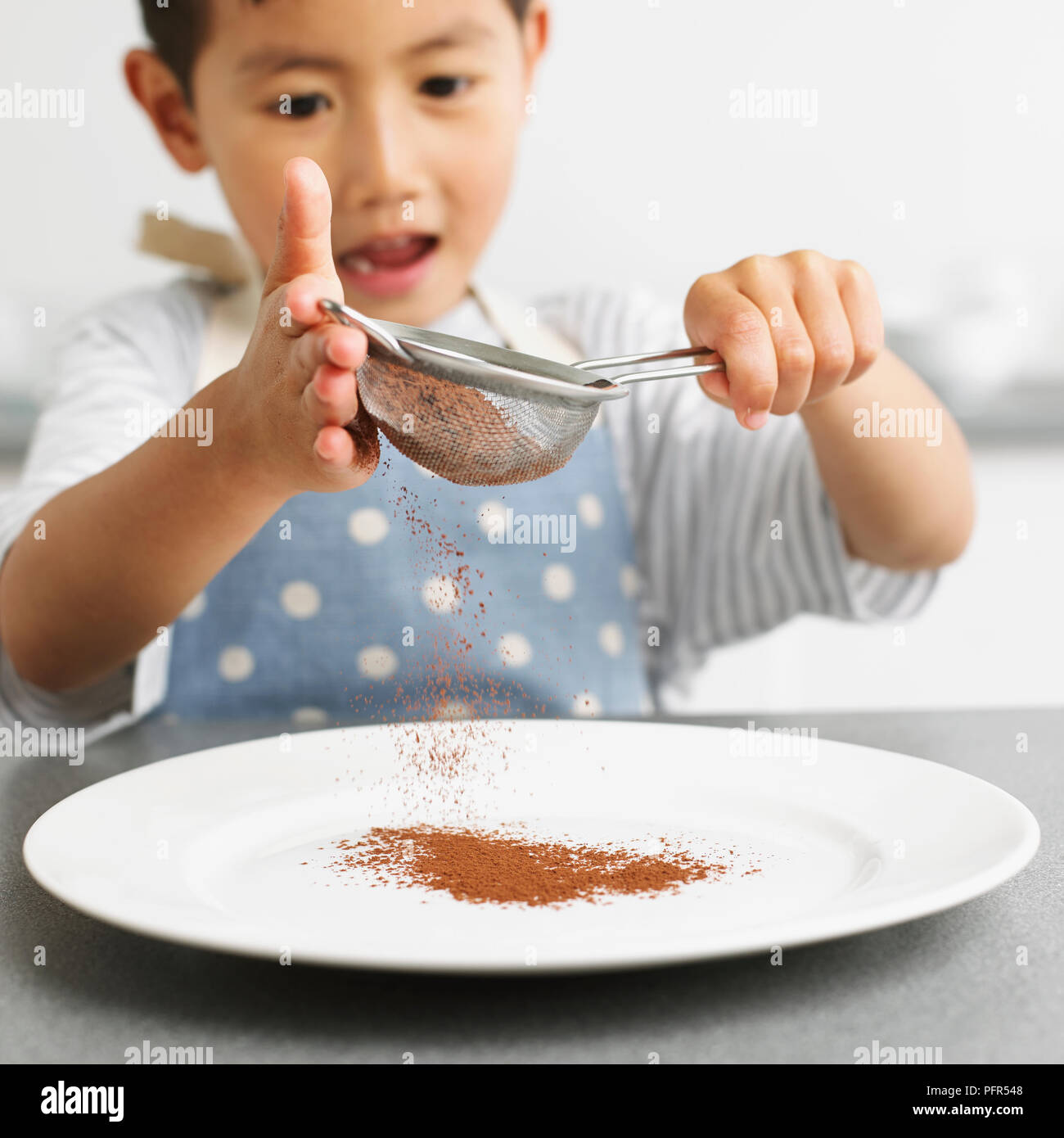 Garçon tamisant le chocolat en poudre sur une assiette, 4 ans Banque D'Images