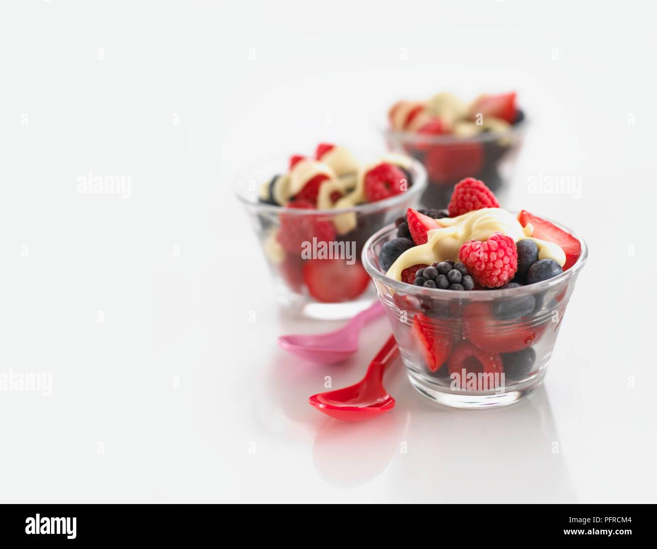 Trois bols en verre contenant des petits fruits d'été et crème, cuillères à proximité Banque D'Images