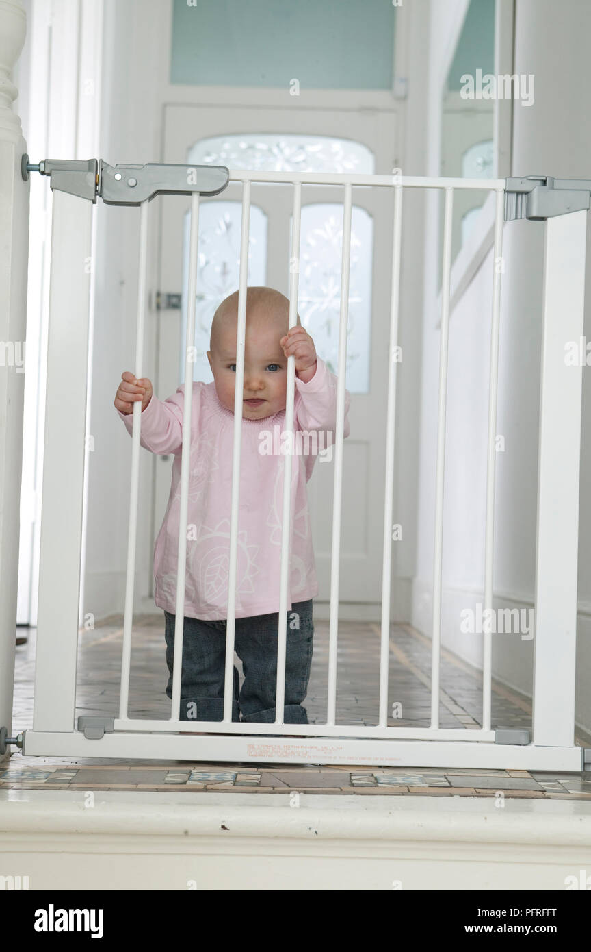 Baby Girl Holding on to porte de sécurité enfant Banque D'Images