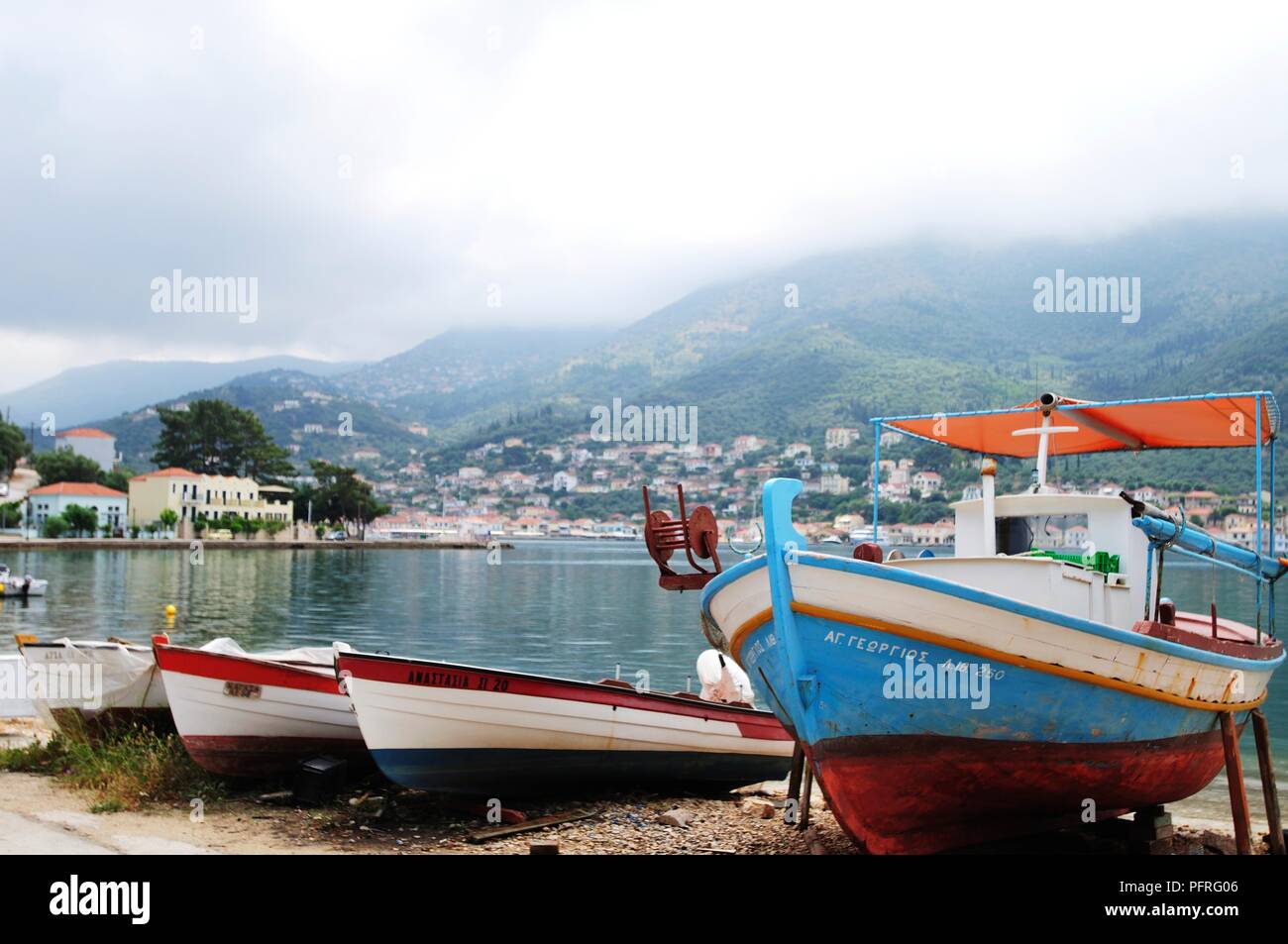 Îles grecques, Ithaque, Vathy, bateaux de pêche amarrés au bord de l'eau avec du brouillard au-dessus de montagnes à distance Banque D'Images