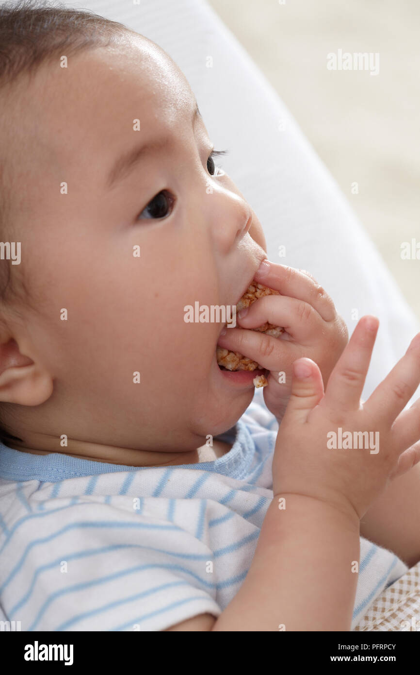 Bébé garçon (6 mois) la farce de la nourriture dans sa bouche Banque D'Images