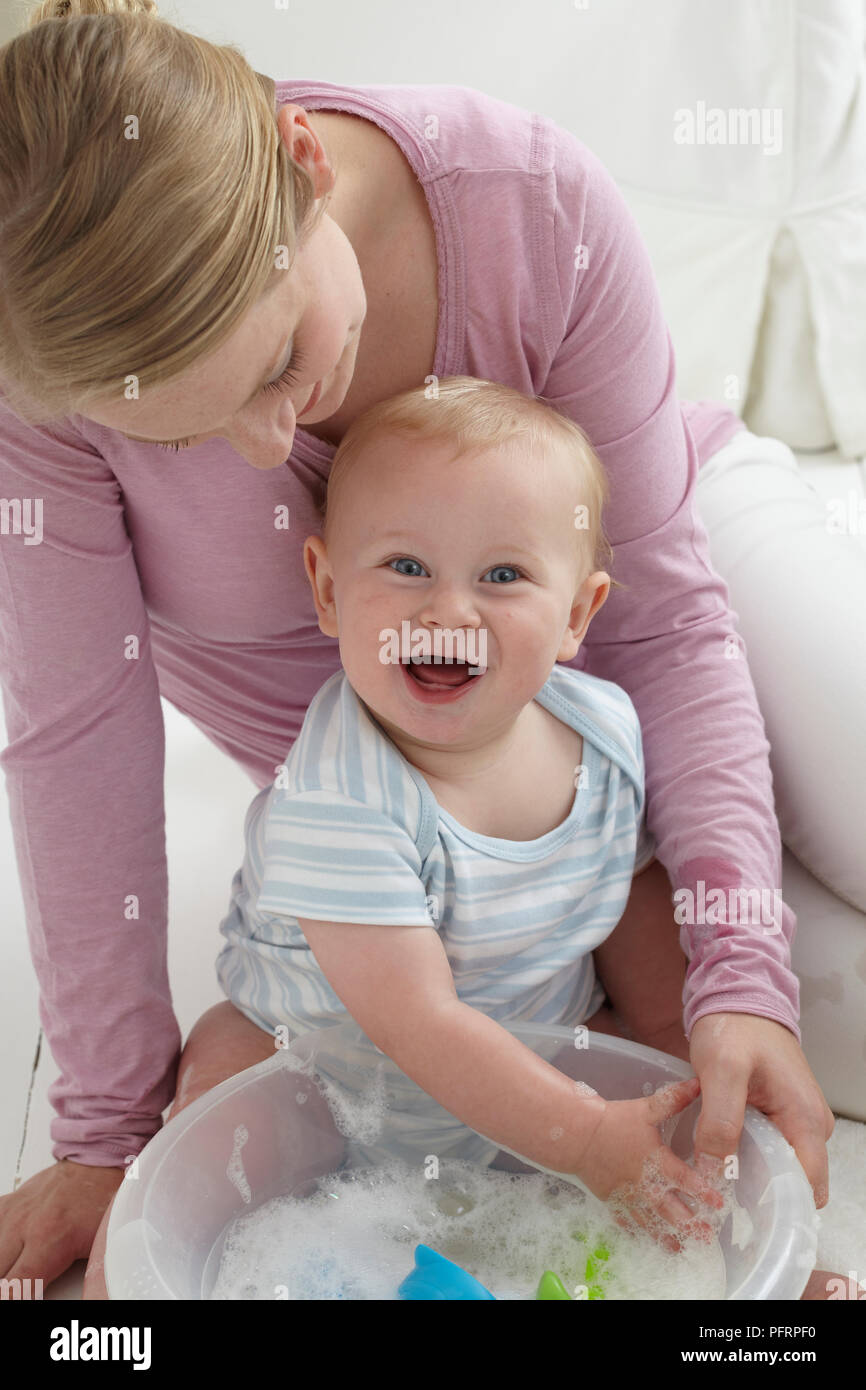 Bebe Garcon 10 Mois A Jouer Avec De L Eau Savonneuse Femme Assise Derriere Lui Photo Stock Alamy
