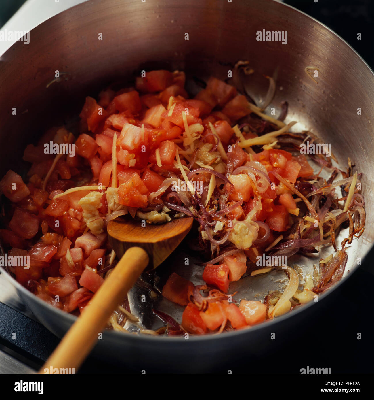 Massalla pakistanais à frire les oignons, les tomates, l'ail et le gingembre dans l'huile chaude dans une casserole avec une cuillère de bois Banque D'Images