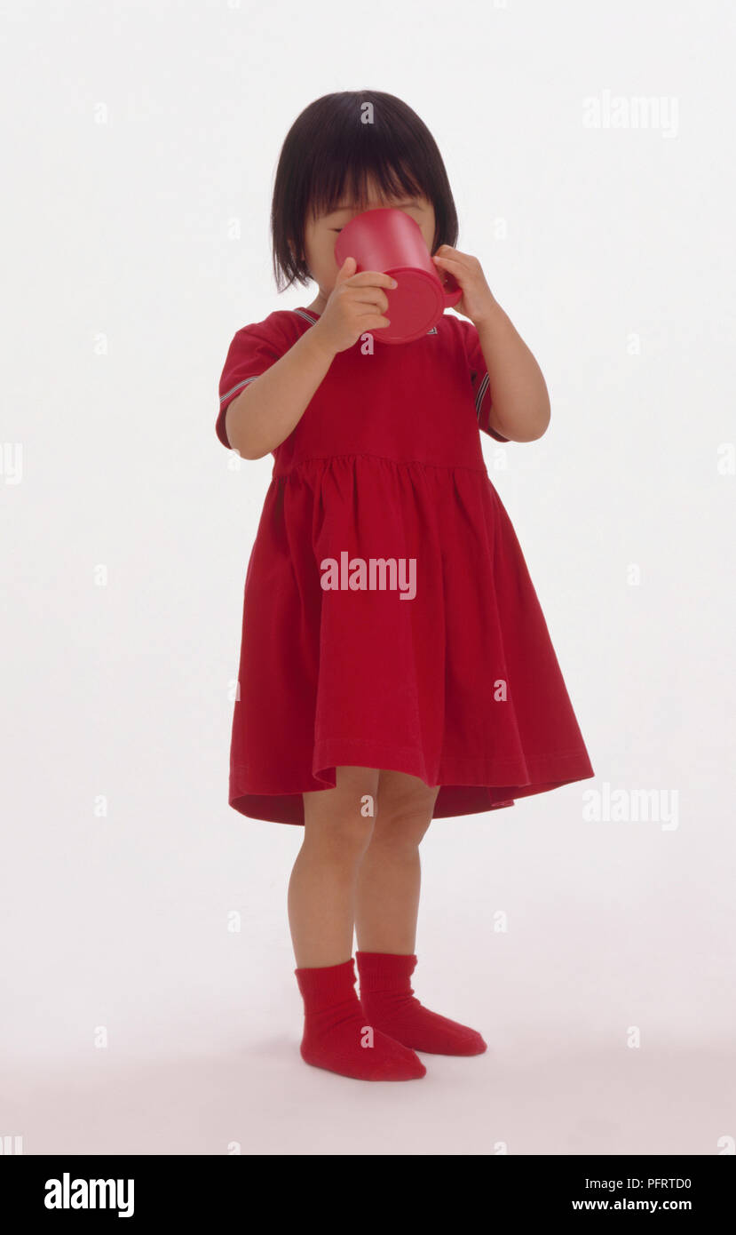 Girl wearing red dress et chaussettes et permanent de potable grande tasse en plastique Banque D'Images