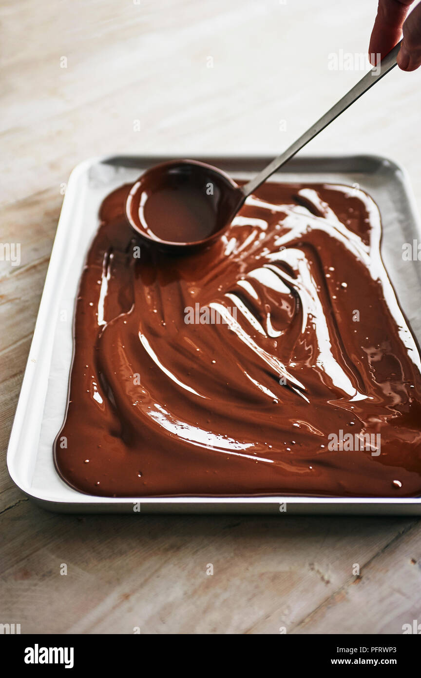 Faire le chocolat noir de l'écorce, répandre le chocolat fondu sur le bac Banque D'Images