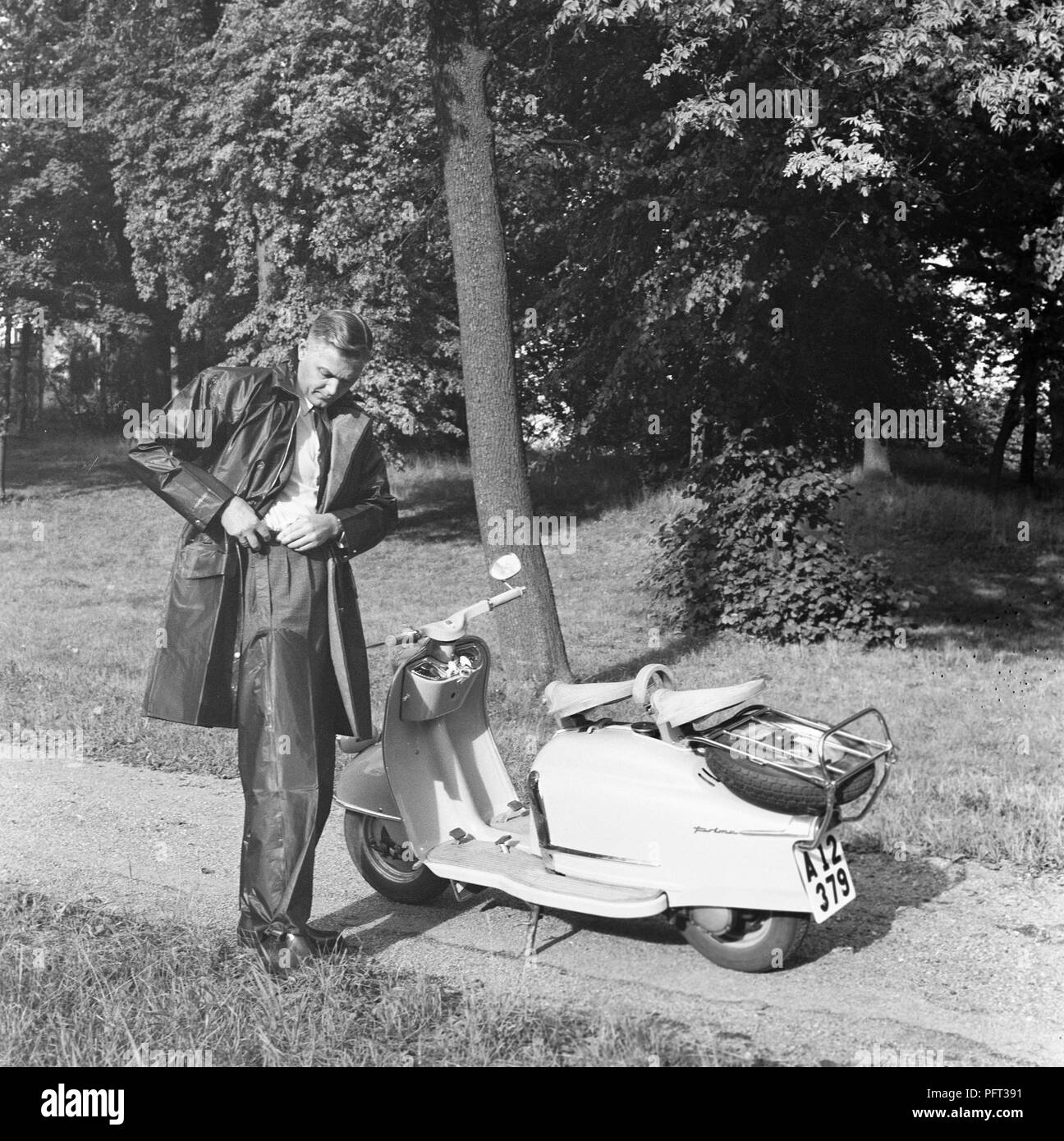 La pluie dans les années 1950. Un jeune homme se prépare pour une tournée sur sa moto scooter NSU prima. Il s'habille dans un imperméable et pantalons imperméables. La Suède Septembre 1959 Banque D'Images