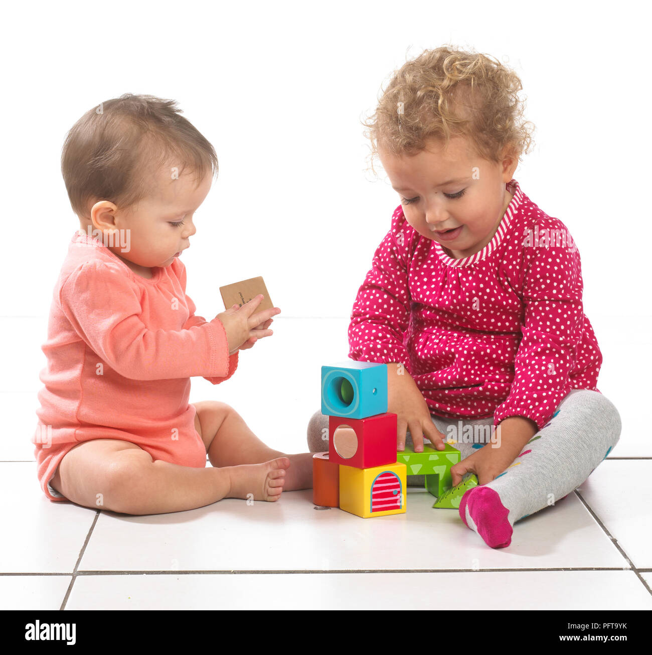 Bébé fille (8 mois) et bébé fille (2 ans) assis à jouer avec des blocs de construction Banque D'Images