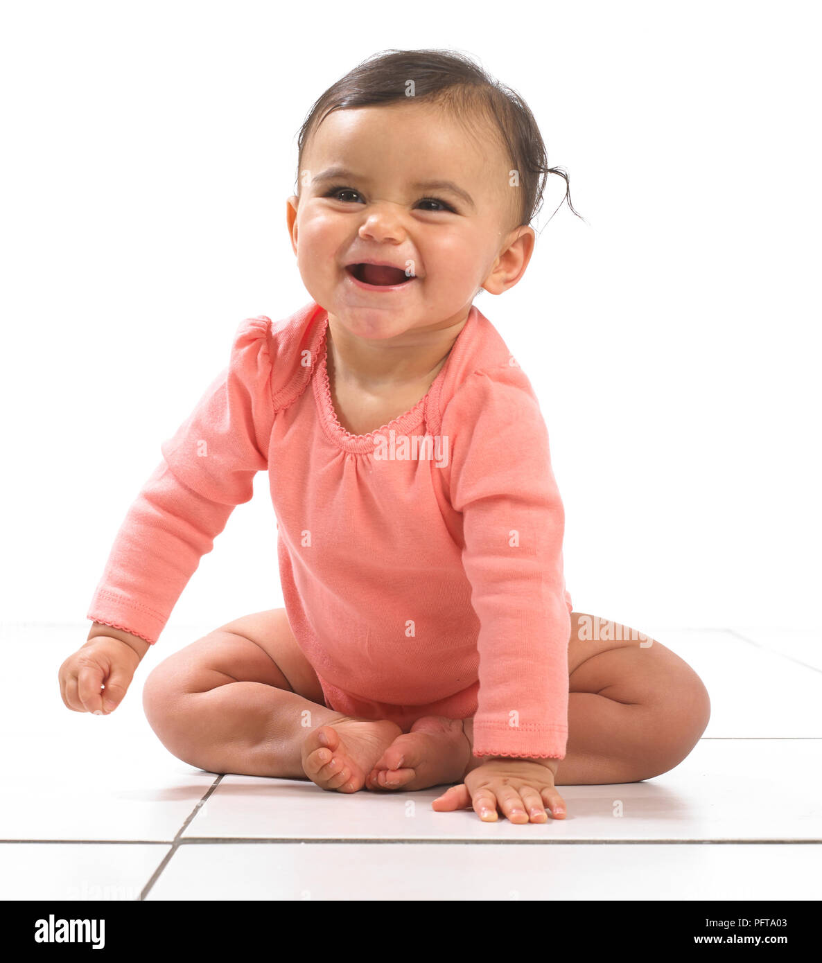 Baby Girl sitting penchée en avant, à rire, à 7 mois Banque D'Images