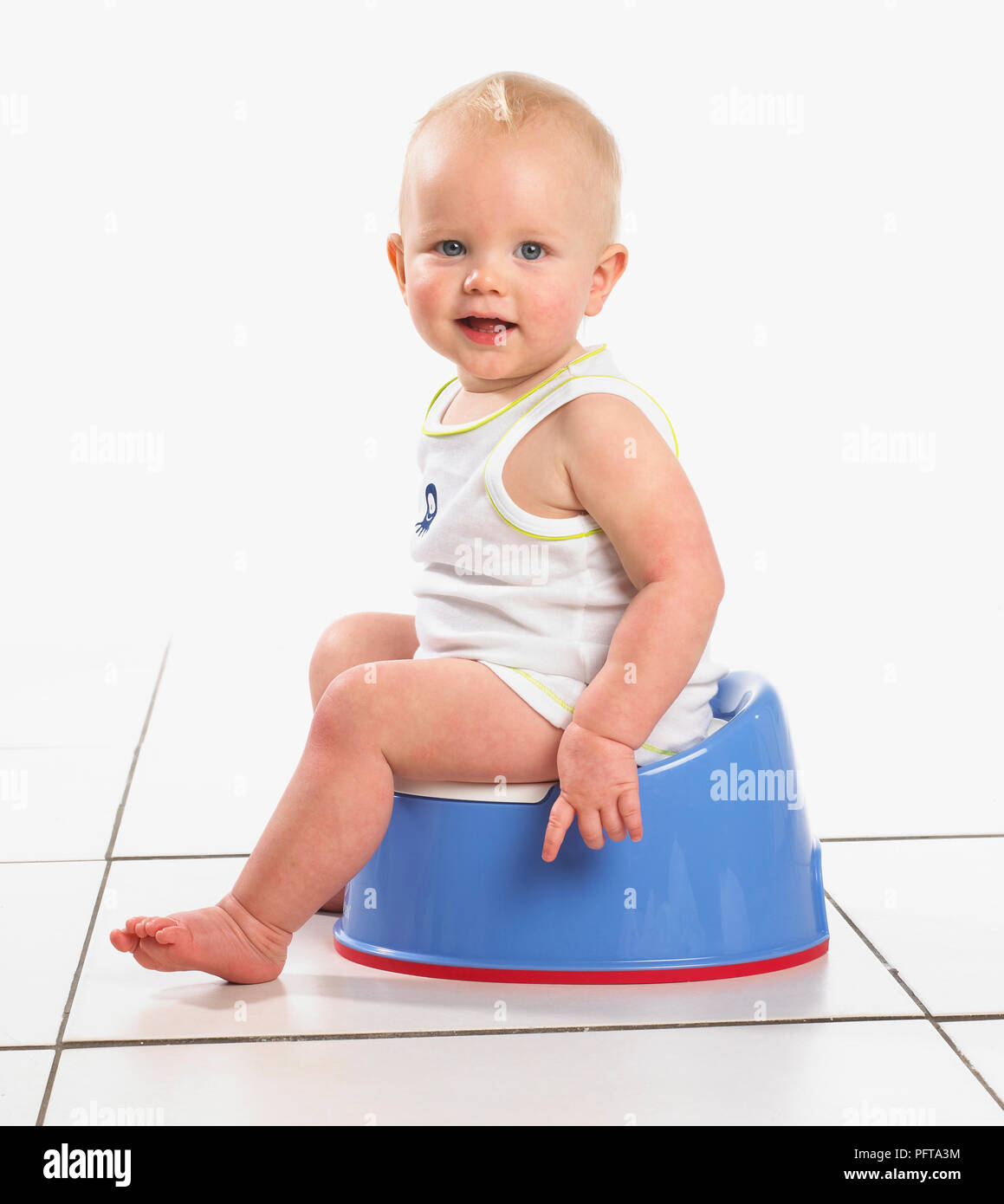 Boy wearing vest assis sur le pot bleu, 15 mois Banque D'Images