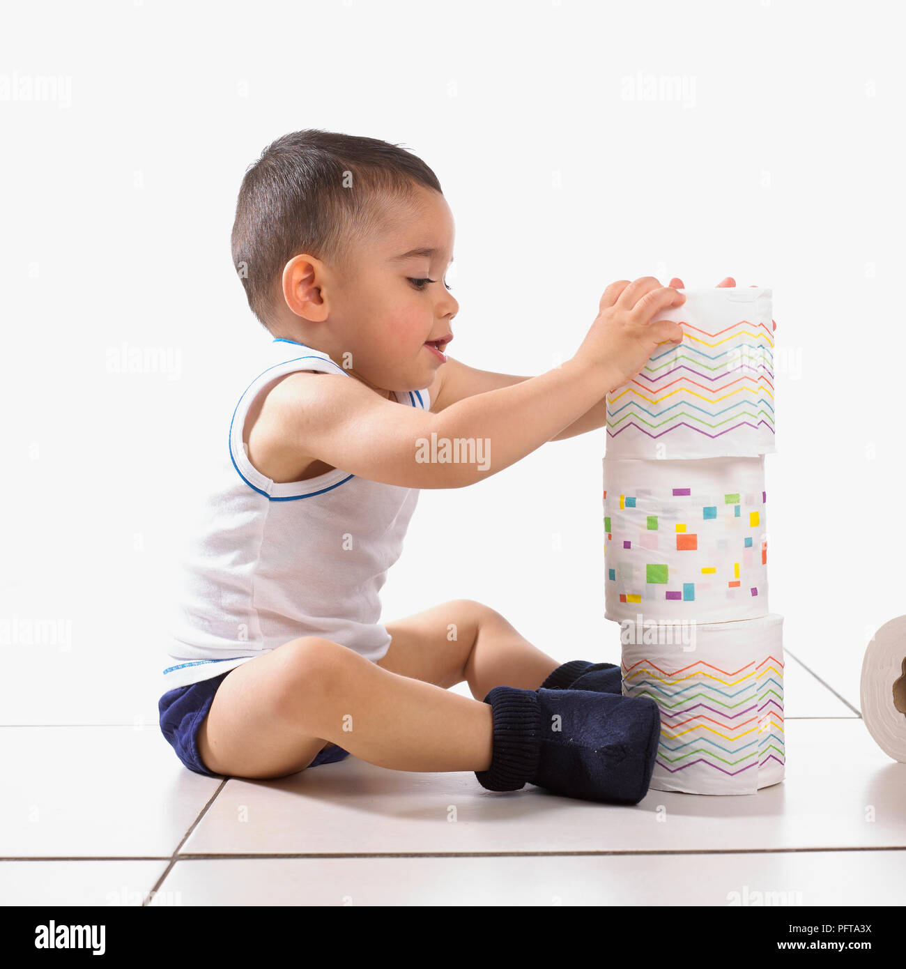 Boy stacking des rouleaux de papier de toilette, 15 mois Banque D'Images