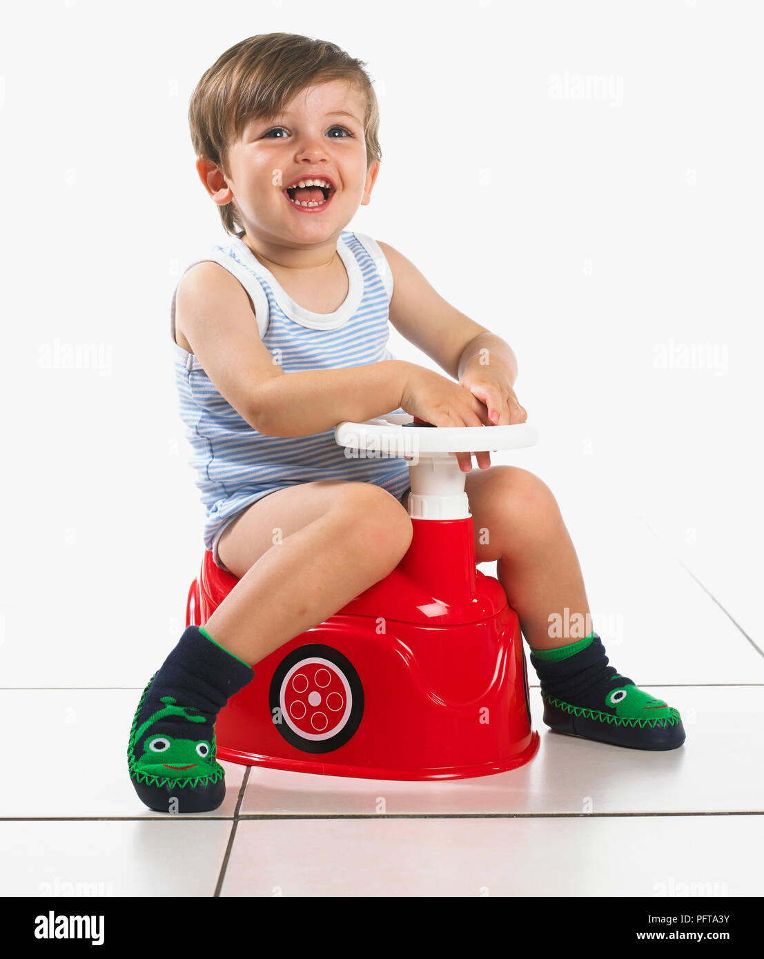 Garçon assis sur un pot en forme de voiture avec volant, 20 mois Banque D'Images