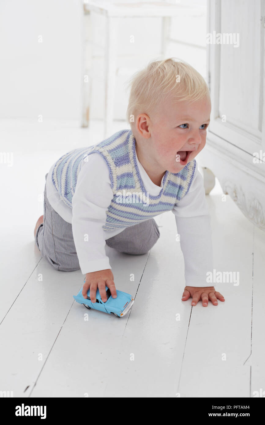 Baby Boy crawling sur marbre Playing with toy voiture, 14 mois Banque D'Images