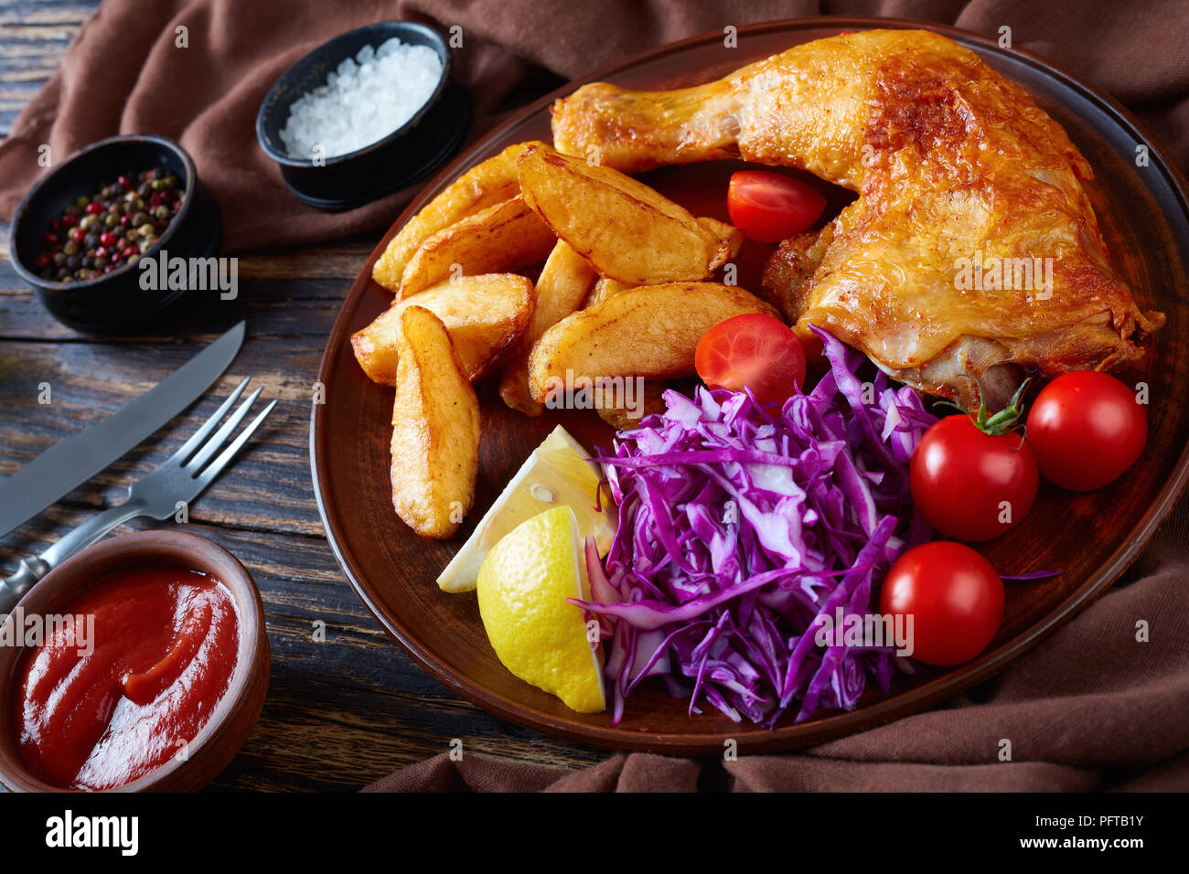 Quartiers de pommes de terre frites, salade de chou et de poulet servi sur une plaque d'argile avec fourchette et couteau rustique sur une table en bois sombre, vue horizontale de la société abo Banque D'Images