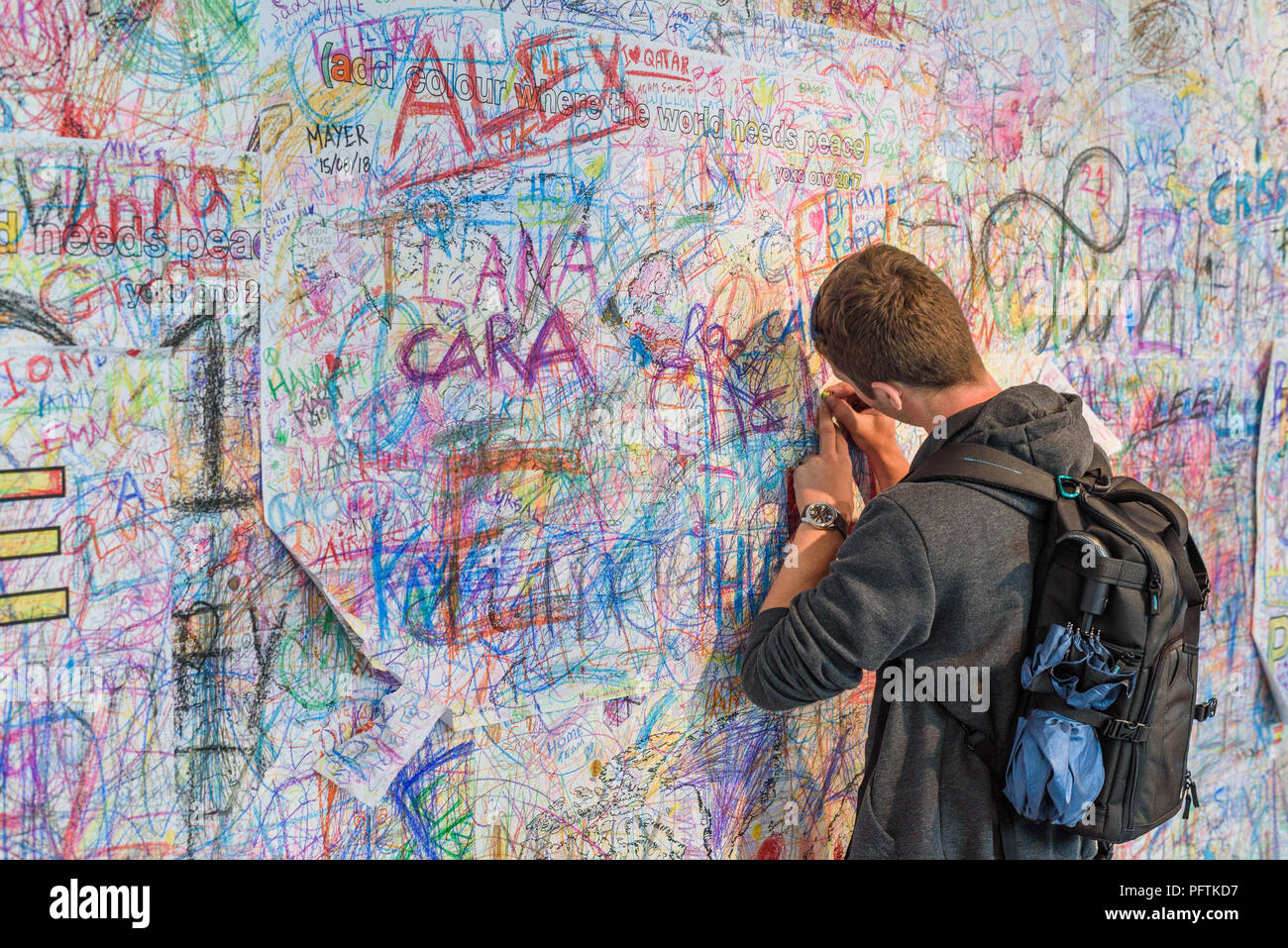 Un jeune homme écrit sur le mur de la paix par Yoko Ono à 'Ajouter couleur où le monde a besoin de la paix" à l'exposition "Double Fantasy" à Liverpool Banque D'Images