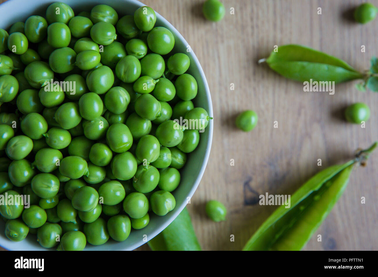 Un plein bol de petits pois frais, jardin biologique qui ont été fraîchement cueilli et retirés de leurs gousses sur une table en bois rustique. Banque D'Images
