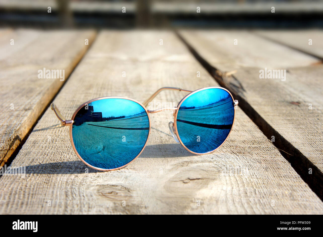 Miroir à la mode lunettes avec verres bleus sur le soleil se coucher sur un sol en bois reste voyage reflète dans verres Banque D'Images