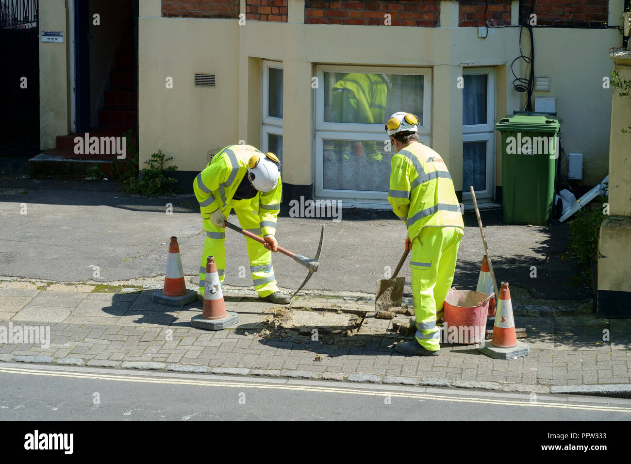 Ouvriers portant des vêtements de sécurité haute visibilité effectuer des réparations à un couvercle de vidange sur un trottoir en angleterre southsea Banque D'Images
