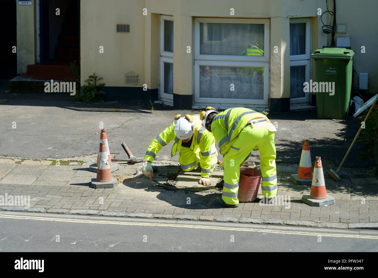 Ouvriers portant des vêtements de sécurité haute visibilité effectuer des réparations à un couvercle de vidange sur un trottoir en angleterre southsea Banque D'Images