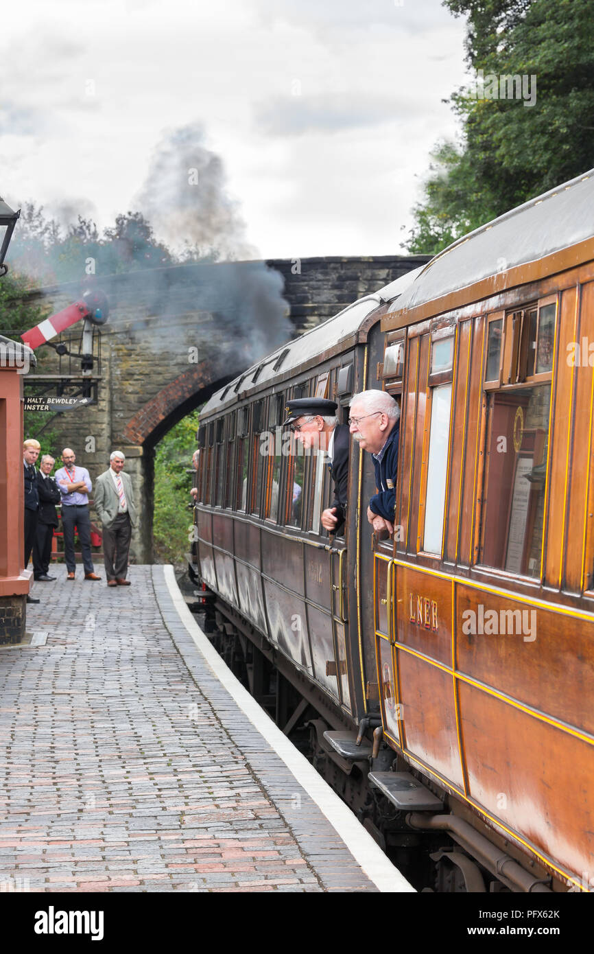Severn Valley Railway steam train attend à vintage UK gare Arley, soufflant de la fumée comme garde & passager stick leurs têtes hors de la fenêtre transport. Banque D'Images