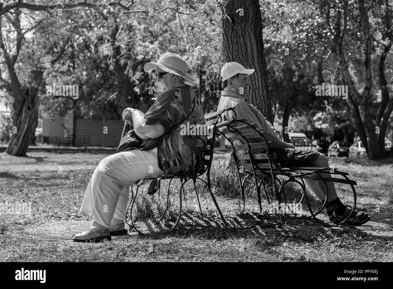 Platia Leonidou Vlachou, Corfu Town, aka Kerkyra, la Grèce : un couple d'ignorer l'un l'autre sur deux bancs de parc. Version noir et blanc Banque D'Images