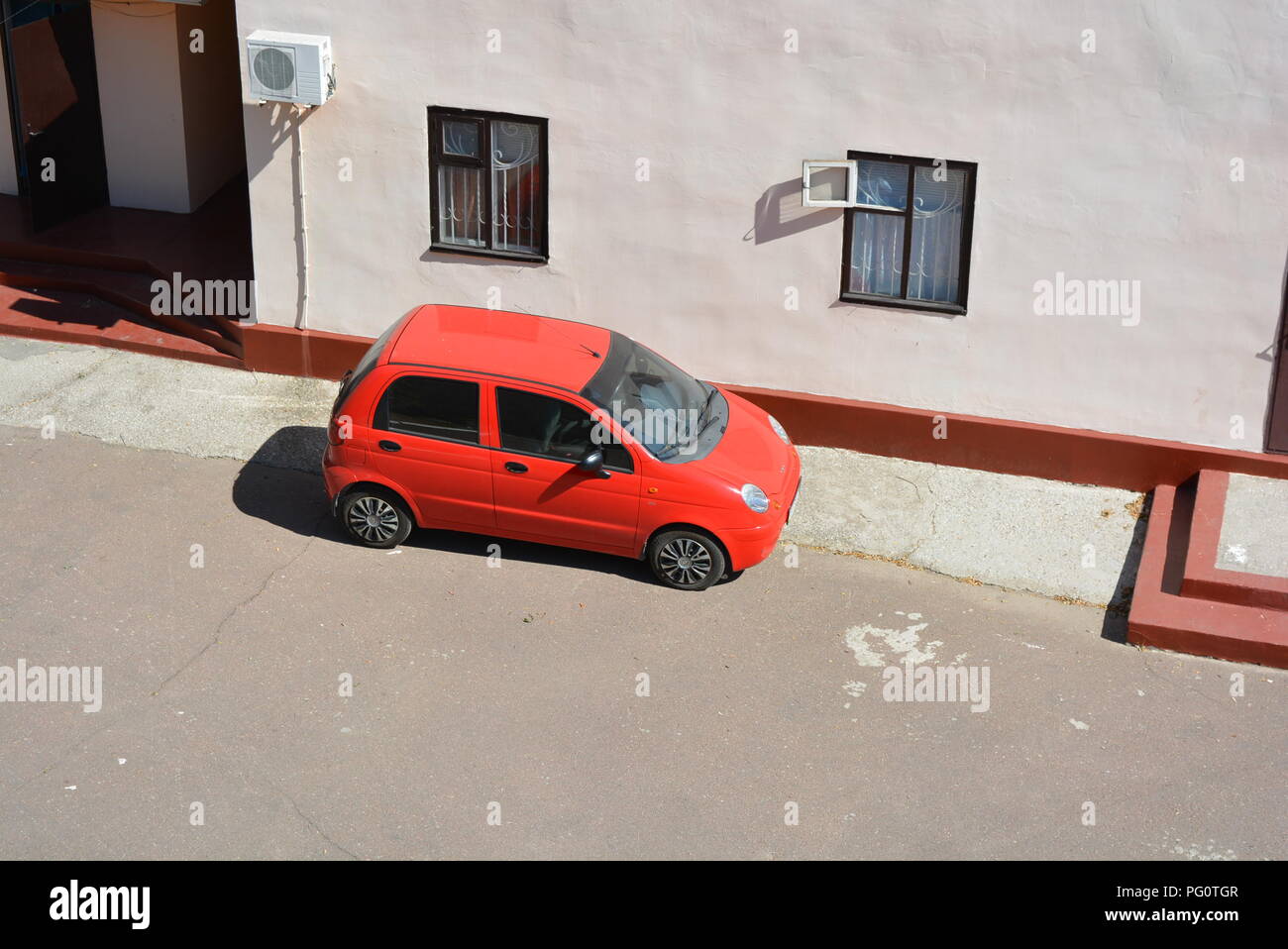 Voiture rouge à quatre portes sur un bâtiment rose avec des rayons de soleil brillants Banque D'Images