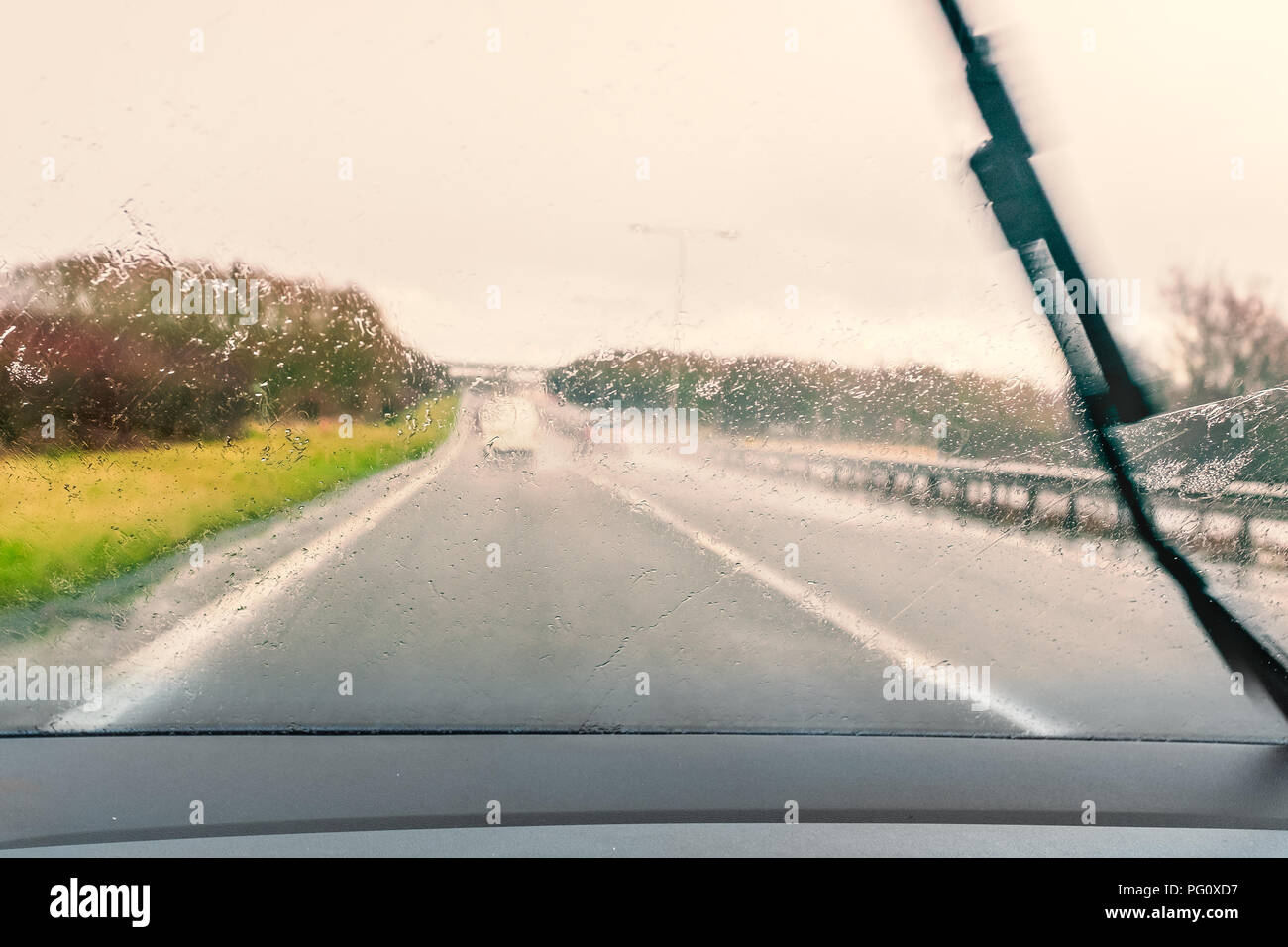 Road vu à travers un pare-brise humide pendant la conduite sous la pluie. Un essuie-glace peut être vu se déplaçant à travers le pare-brise Banque D'Images