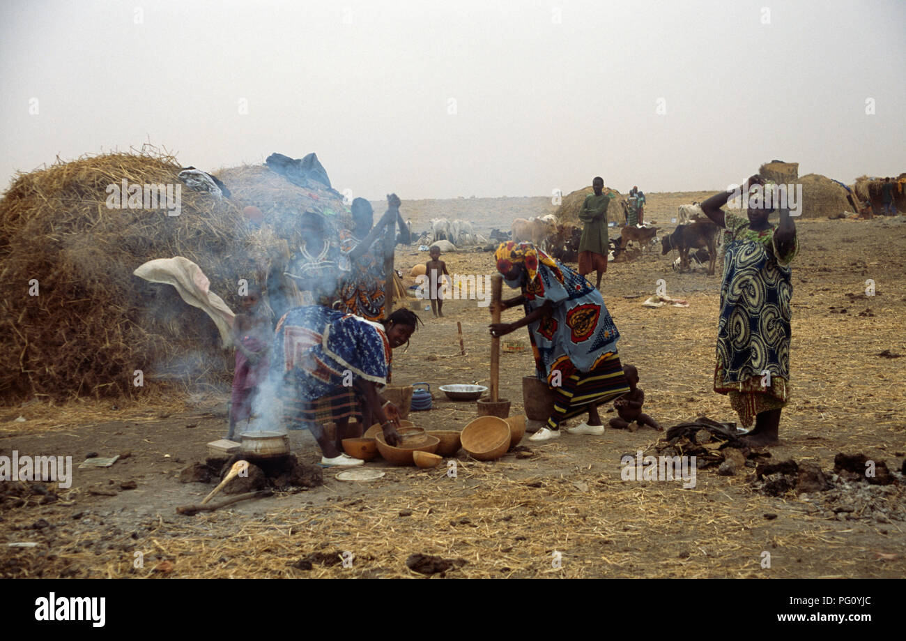 Piler le mil à côté de la cheminée à foyer ouvert dans le campement Peul, Mopti au Mali pour un usage éditorial uniquement Banque D'Images