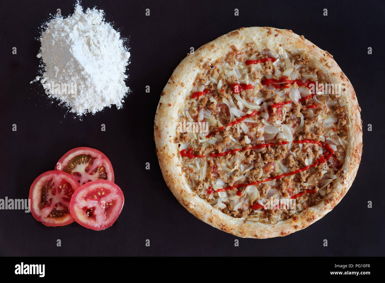 Thon au four pizza, tas de farine et de tranches de tomate sur fond noir Banque D'Images