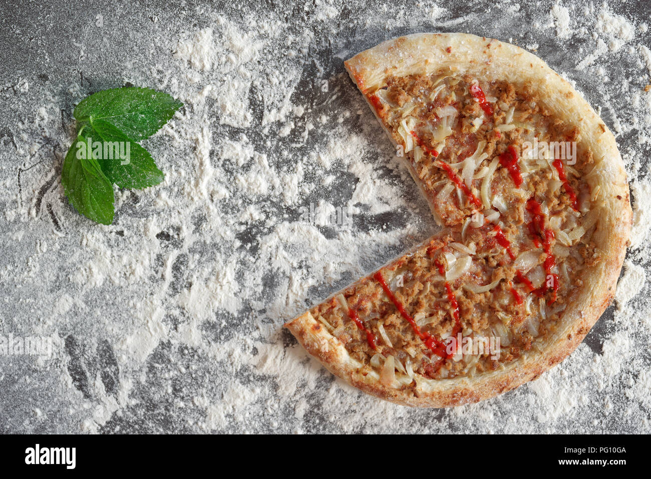 Pizza au thon cuit et feuilles vertes sur fond sombre parsemée de farine blanche Banque D'Images