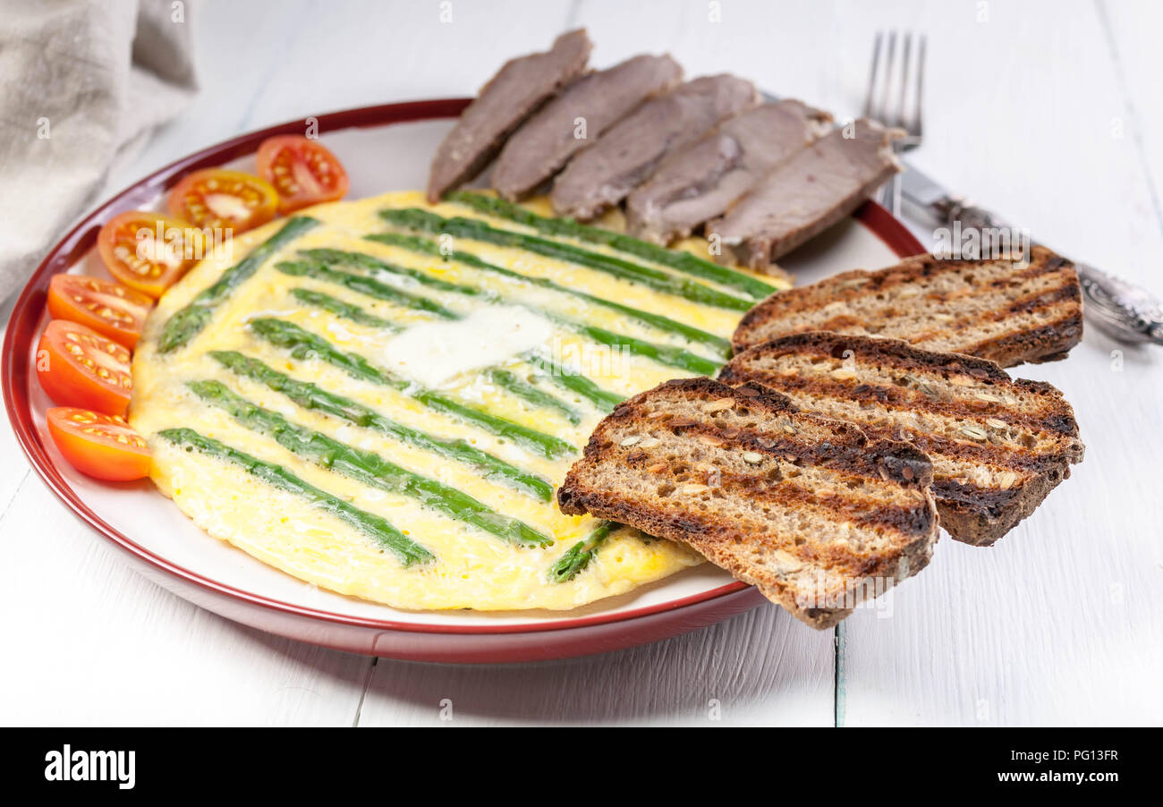 Omelette aux asperges. De jambon, tomates cerise, pain grillé. Fond clair en bois Banque D'Images
