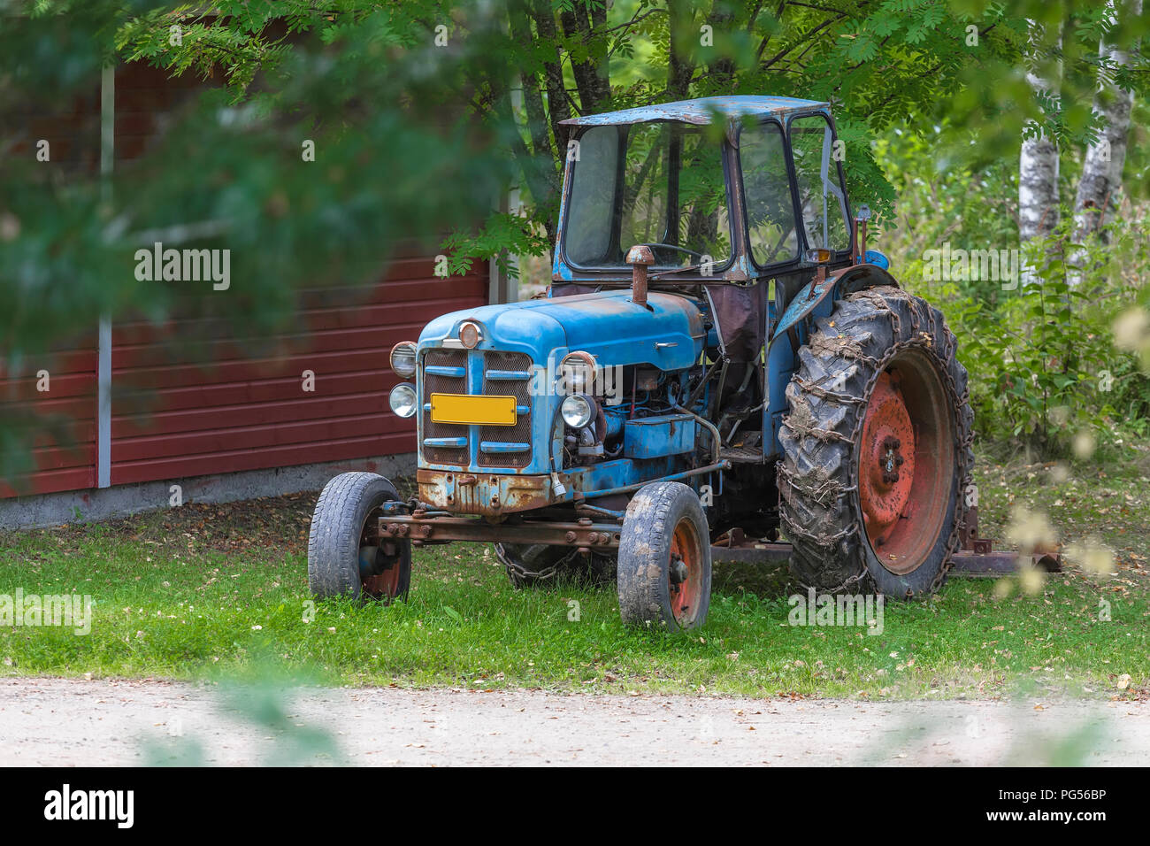 Vieux tracteur avec les chaînes sur les roues debout sous un arbre Banque D'Images