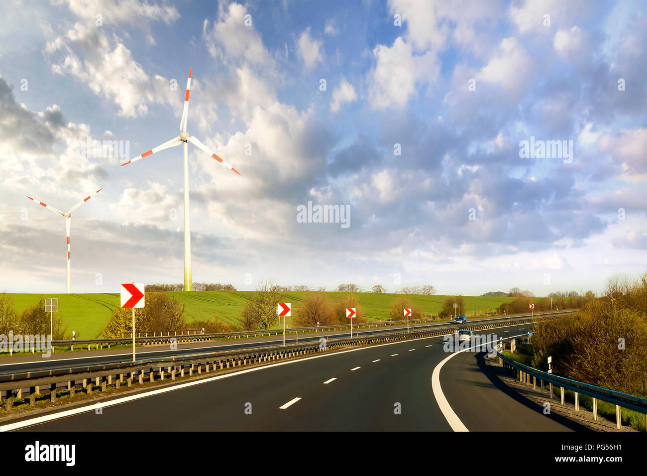 Grande route avec voiture en mouvement qui s'étend à l'horizon de collines vertes avec des éoliennes sur fond de ciel bleu nuageux. Les technologies modernes, renewabl Banque D'Images