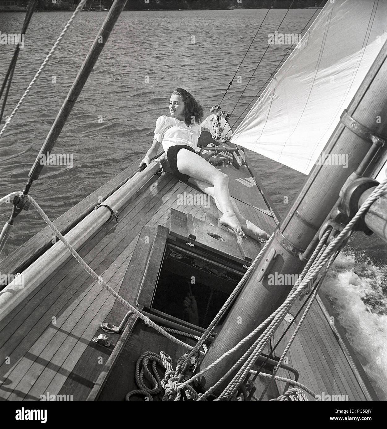 1940 Bateau à voile. Une jeune femme est à bord d'un bateau à voile à la  mode et est couchée sur le pont lorsqu'il cruises avant avec le vent dans  les voiles.