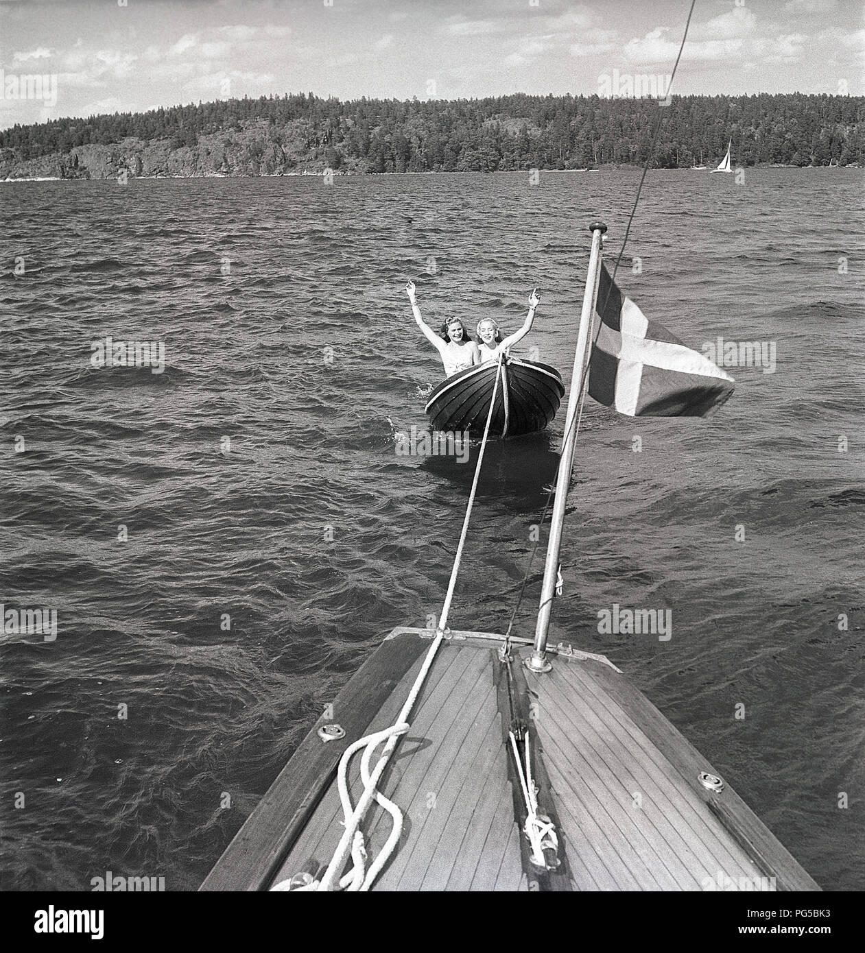 1940 La navigation de plaisance. Deux jeunes femmes sont assis dans le  canot attaché par une ligne à un bateau à voile. Ils portent des années 40  typique maillot de bain et