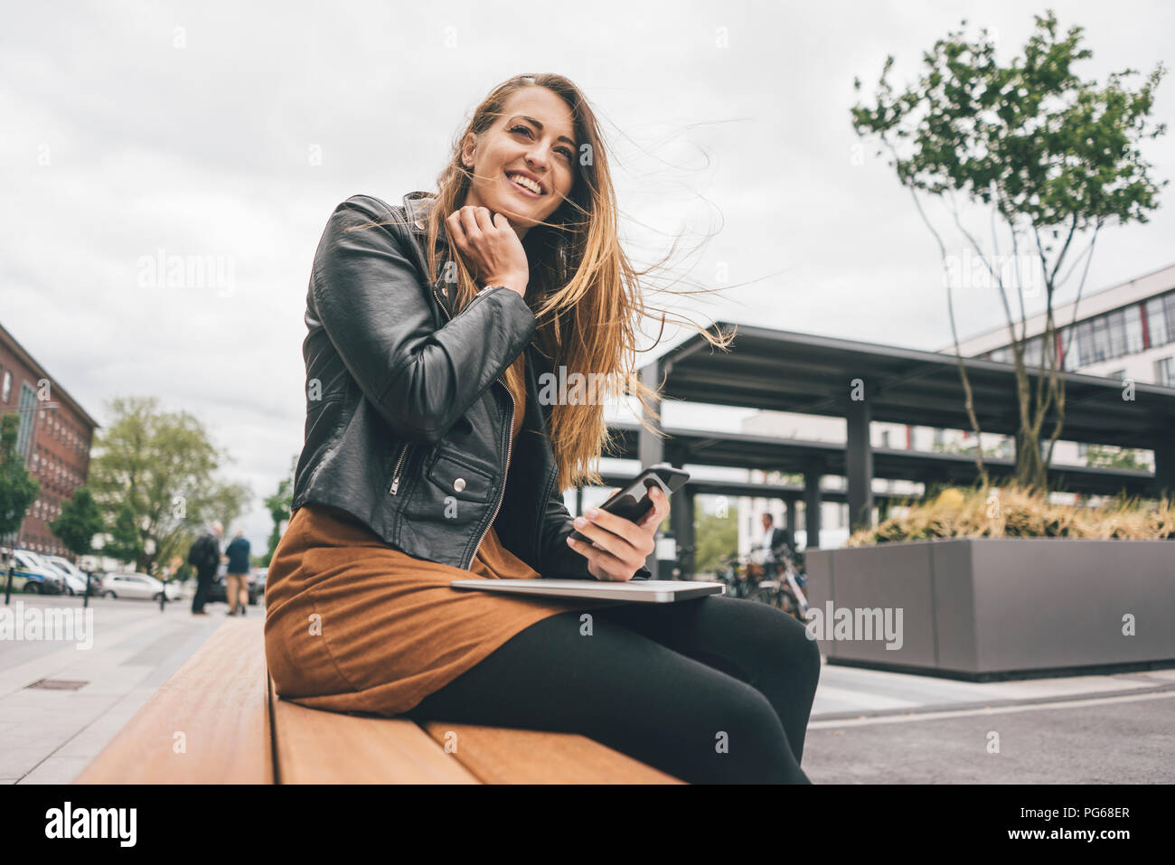 Jeune femme avec un ordinateur portable et un téléphone cellulaire dans la ville Banque D'Images
