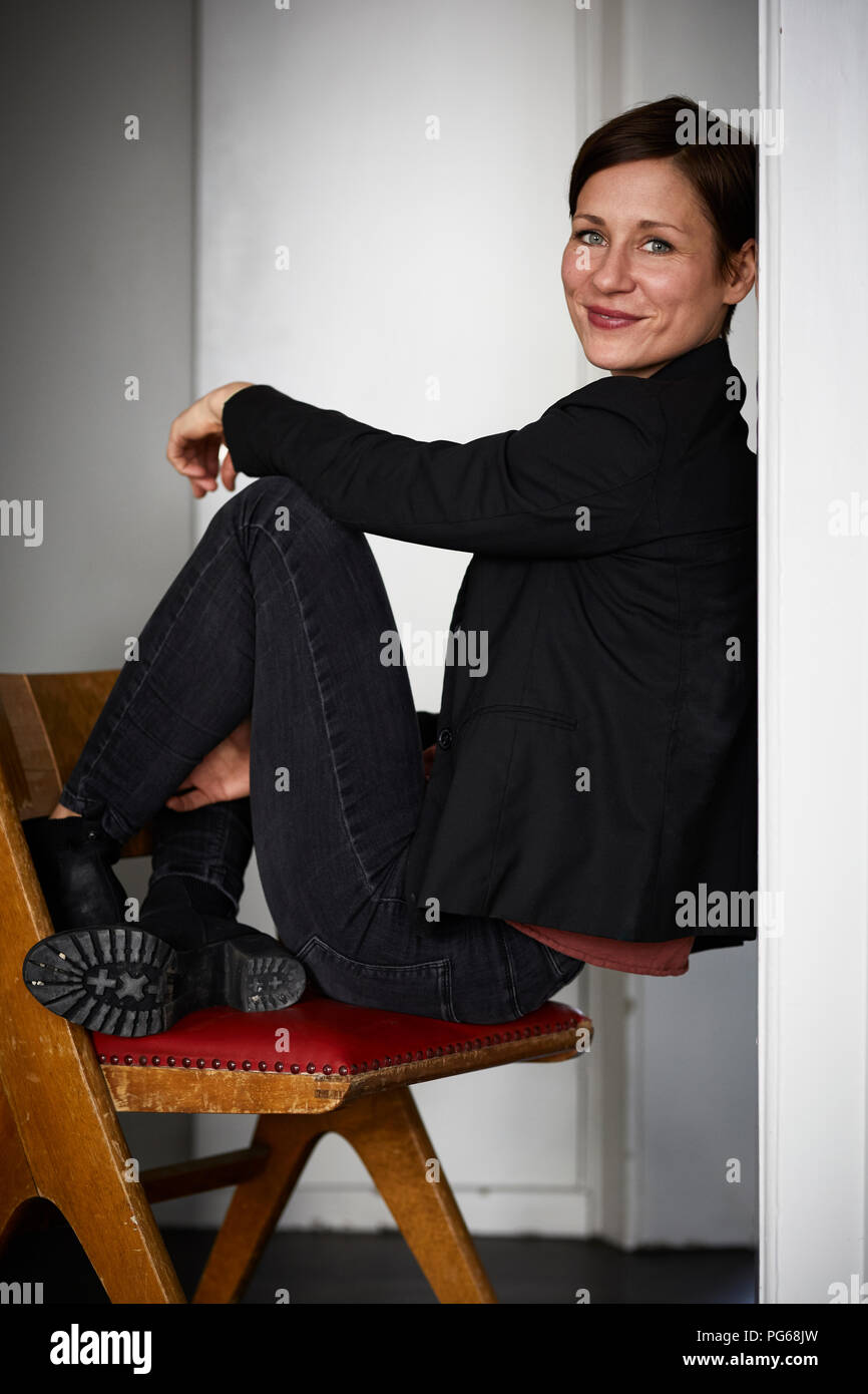 Femme moderne accroupi sur une chaise, leaning on wall Banque D'Images