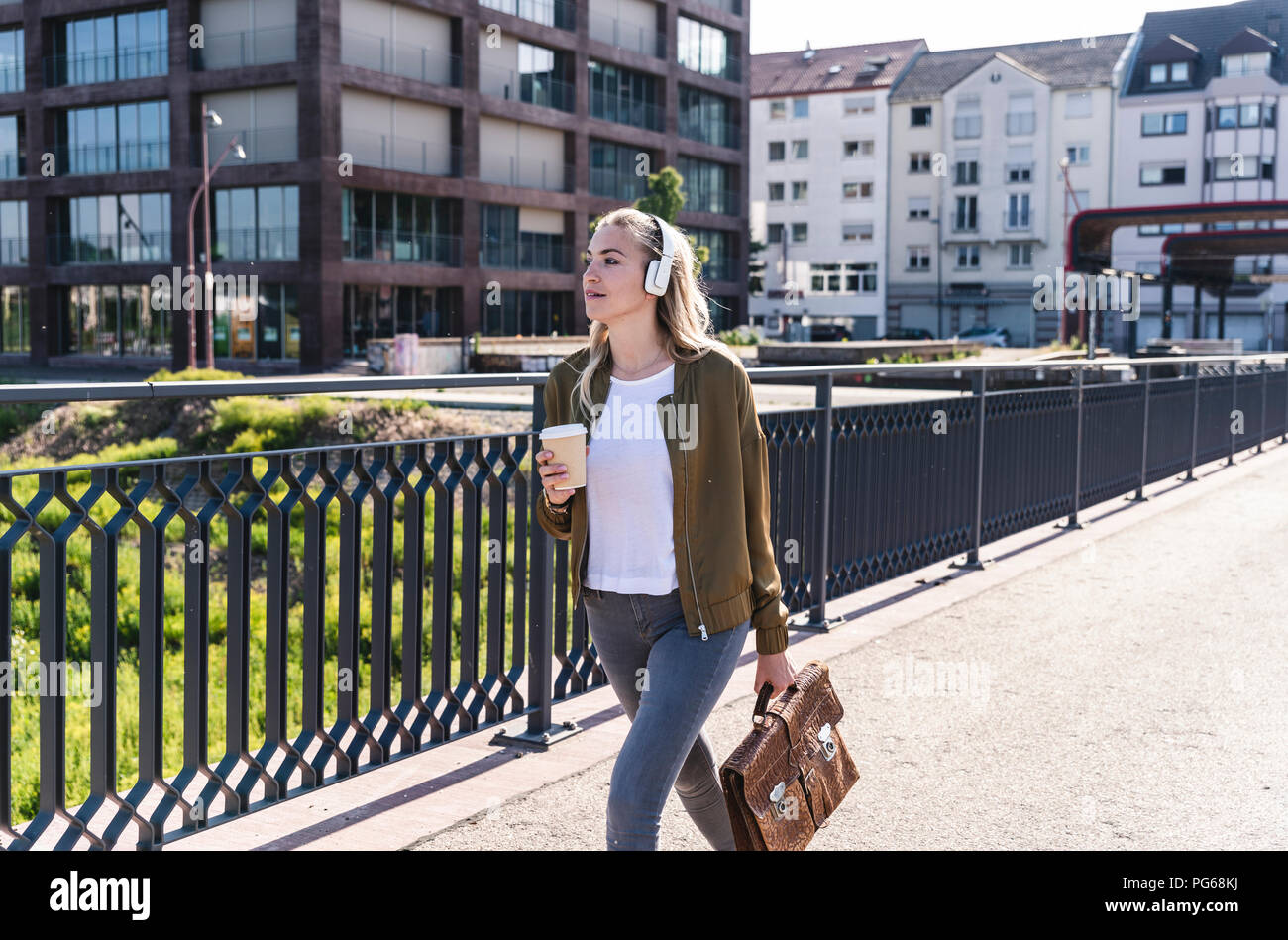 Jeune femme marche sur pont, boire du café, d'écouter de la musique avec des écouteurs Banque D'Images