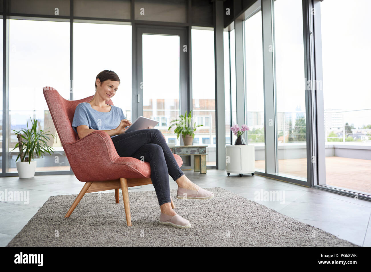 Femme assise dans un fauteuil à la maison à l'aide de tablet Banque D'Images